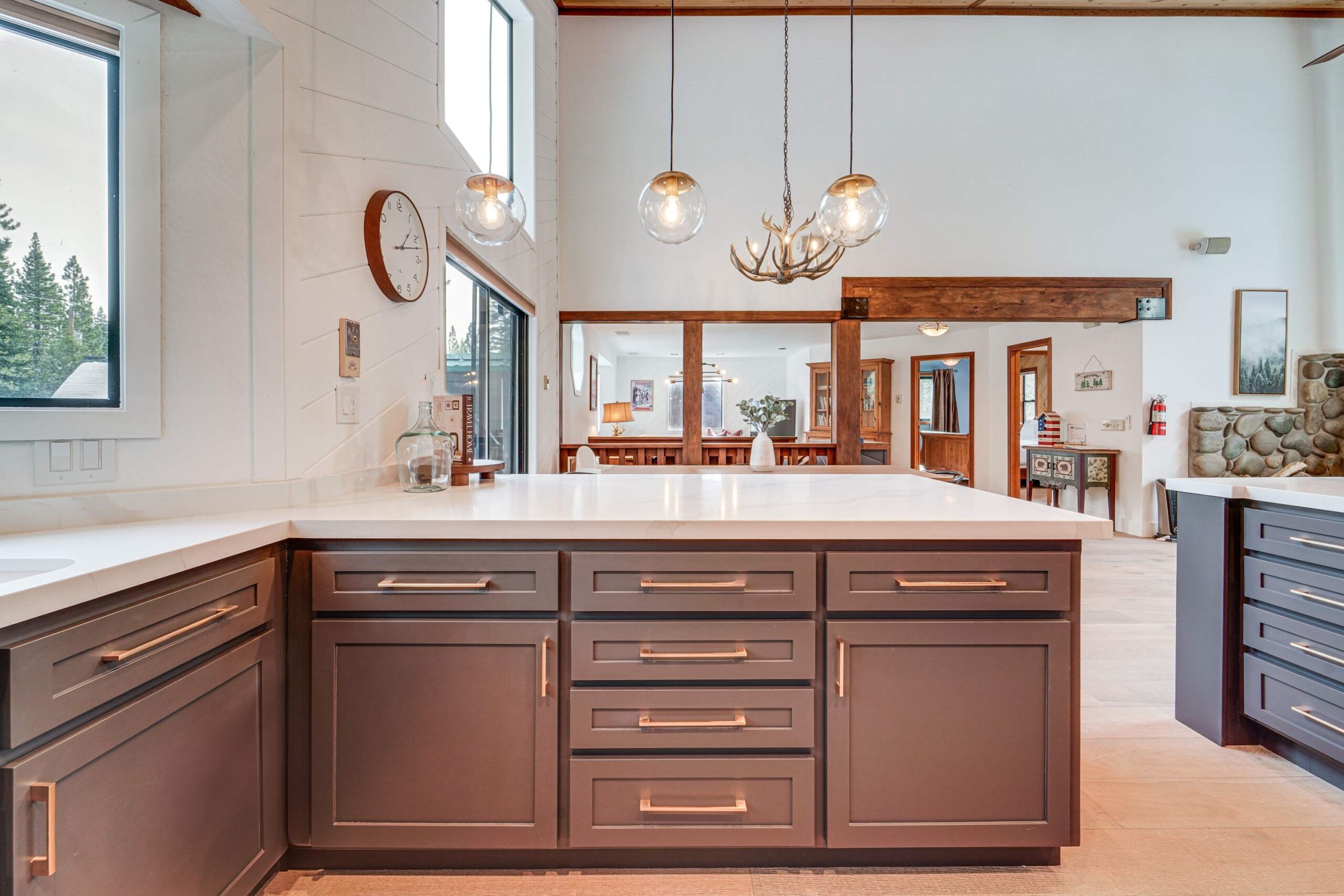 Modern kitchen in a Truckee vacation rental with natural light, antler chandelier, and forest views through large windows.