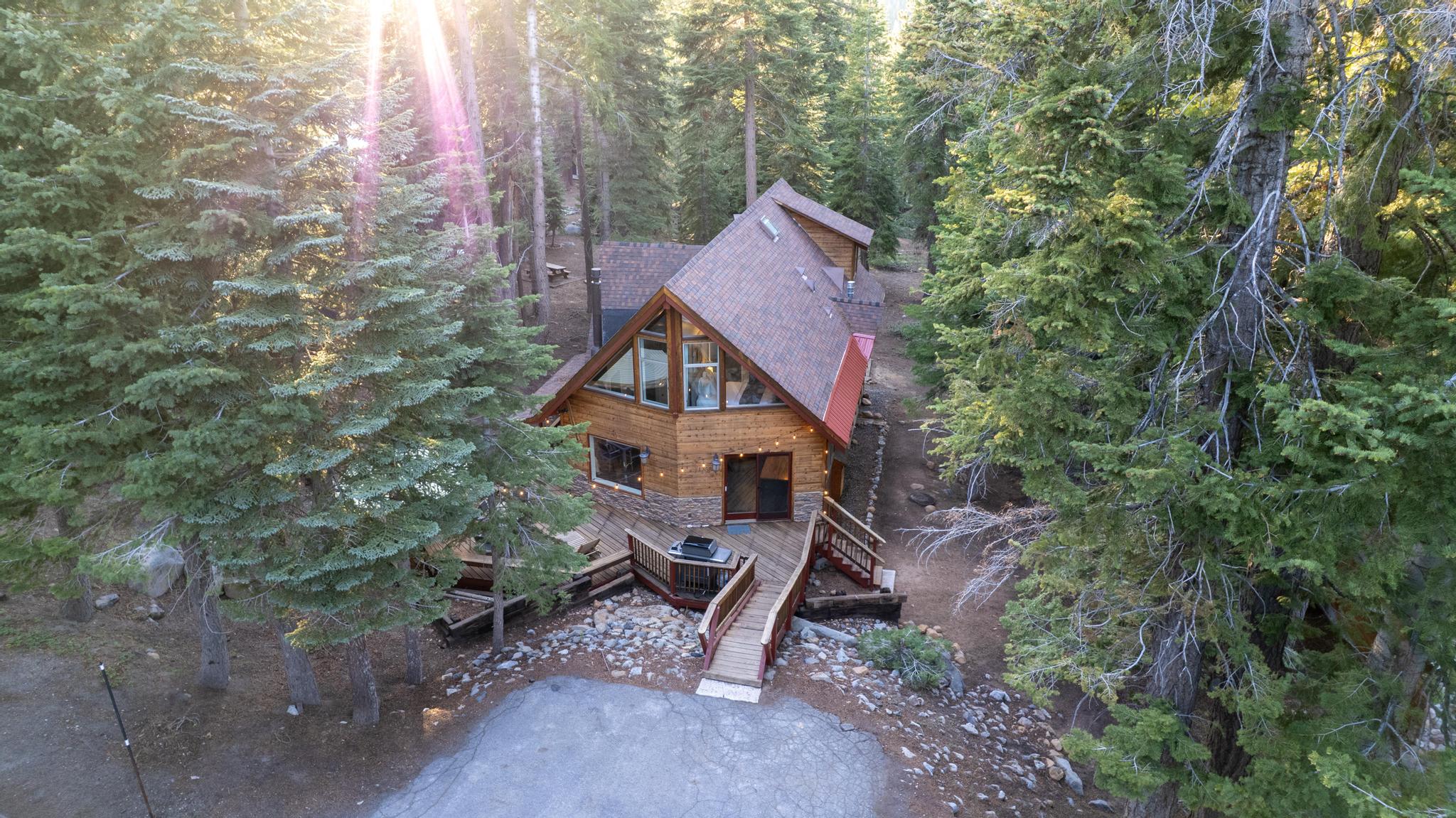 A-Frame cabin amidst lush trees, vacation rental in Tahoe Vista, with sloped roof and sun rays filtering through forest.