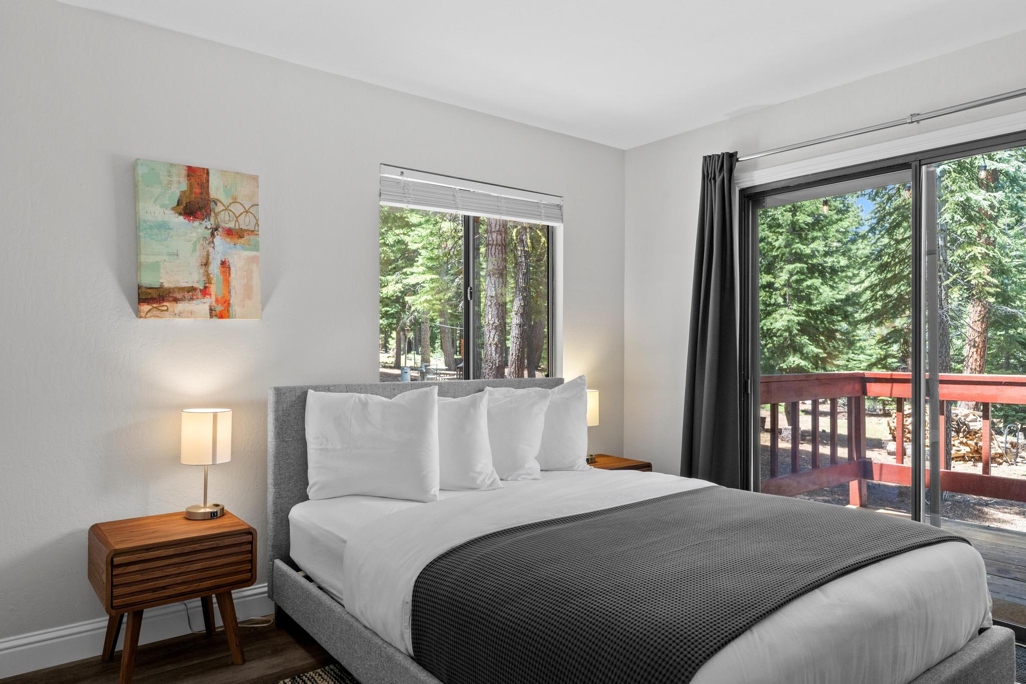 Bedroom in a Tahoe Vista vacation rental with modern decor, large window, and a view of lush trees outside.