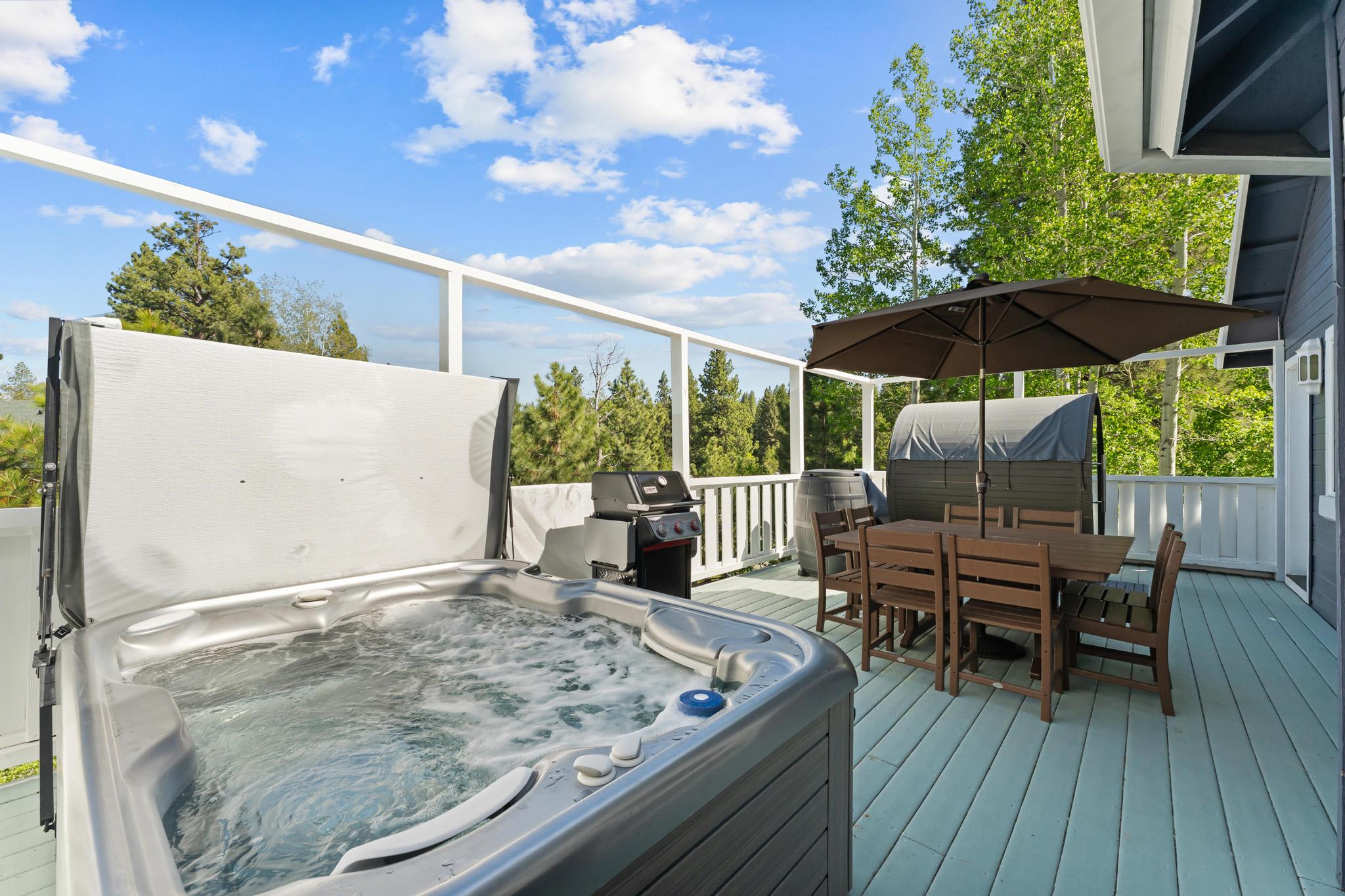 Outdoor deck in Truckee vacation rental with hot tub, BBQ grill, dining table, umbrella, and scenic forest views.