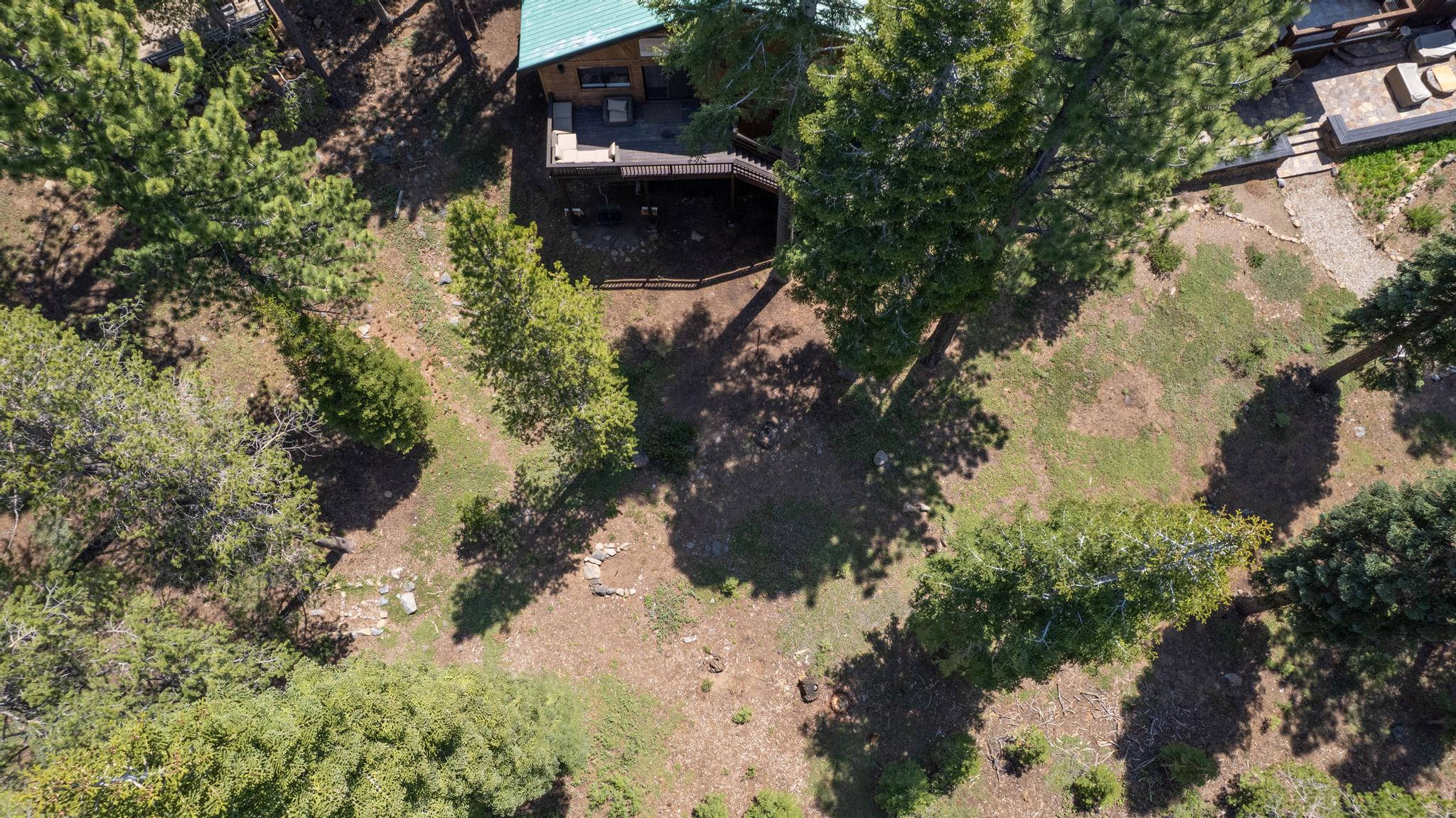 Aerial view of a cozy cabin among trees, Truckee vacation rental with a deck and surrounding forested area.