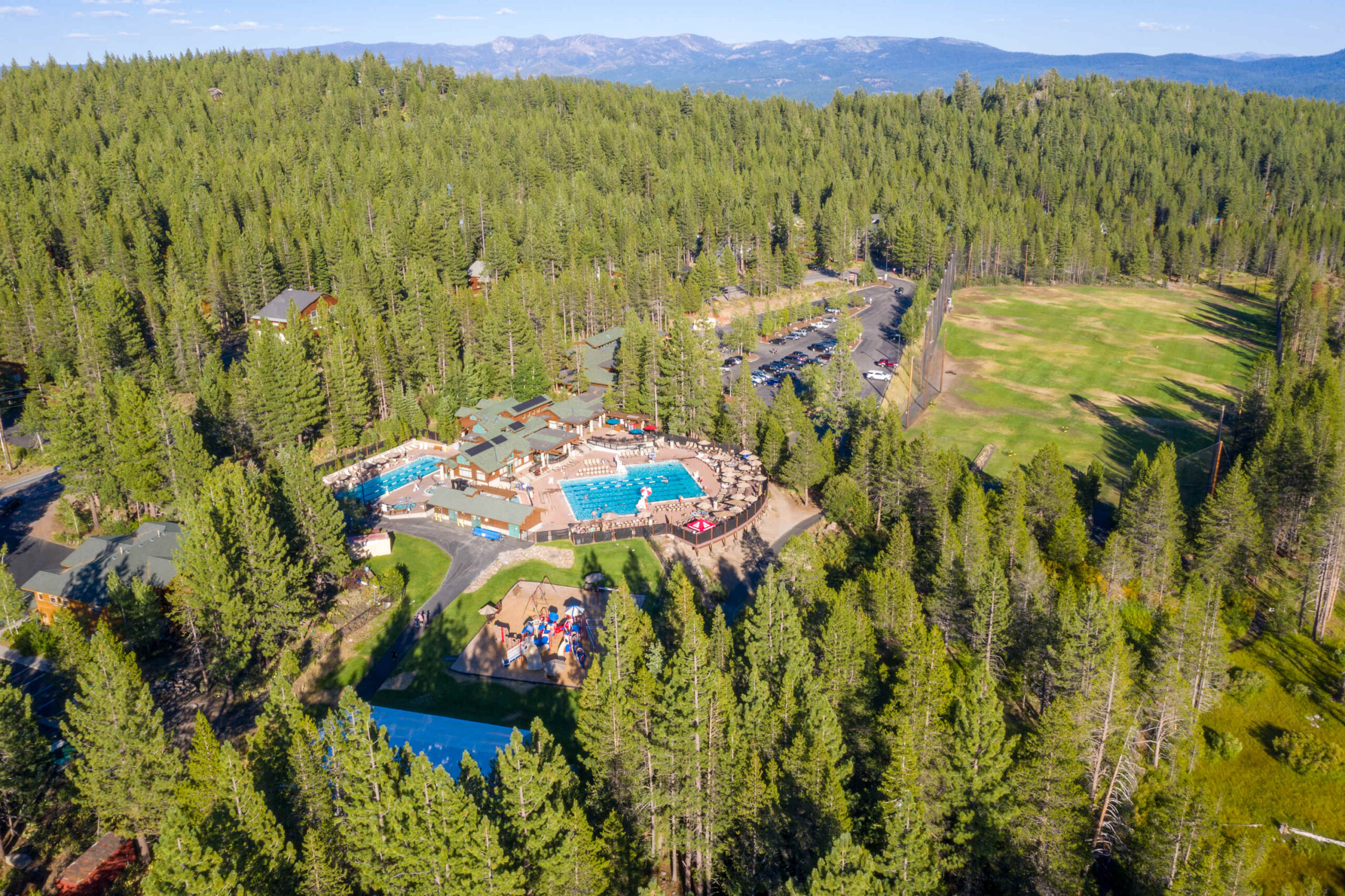 Aerial view of Truckee vacation rental surrounded by forest, featuring a pool complex and large grassy area.