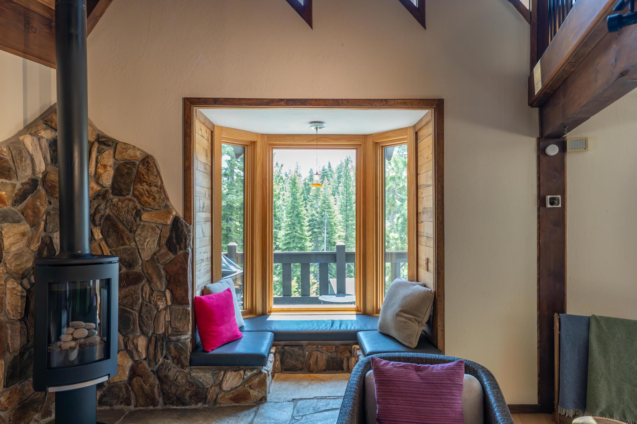 Cozy Tahoe Vista vacation rental with stone fireplace and bay window seating overlooking a forest view.