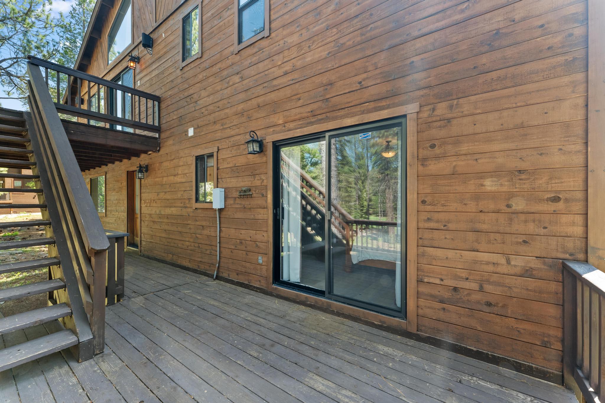 Wooden deck and staircase of a Truckee vacation rental, surrounded by trees and featuring sliding glass doors.