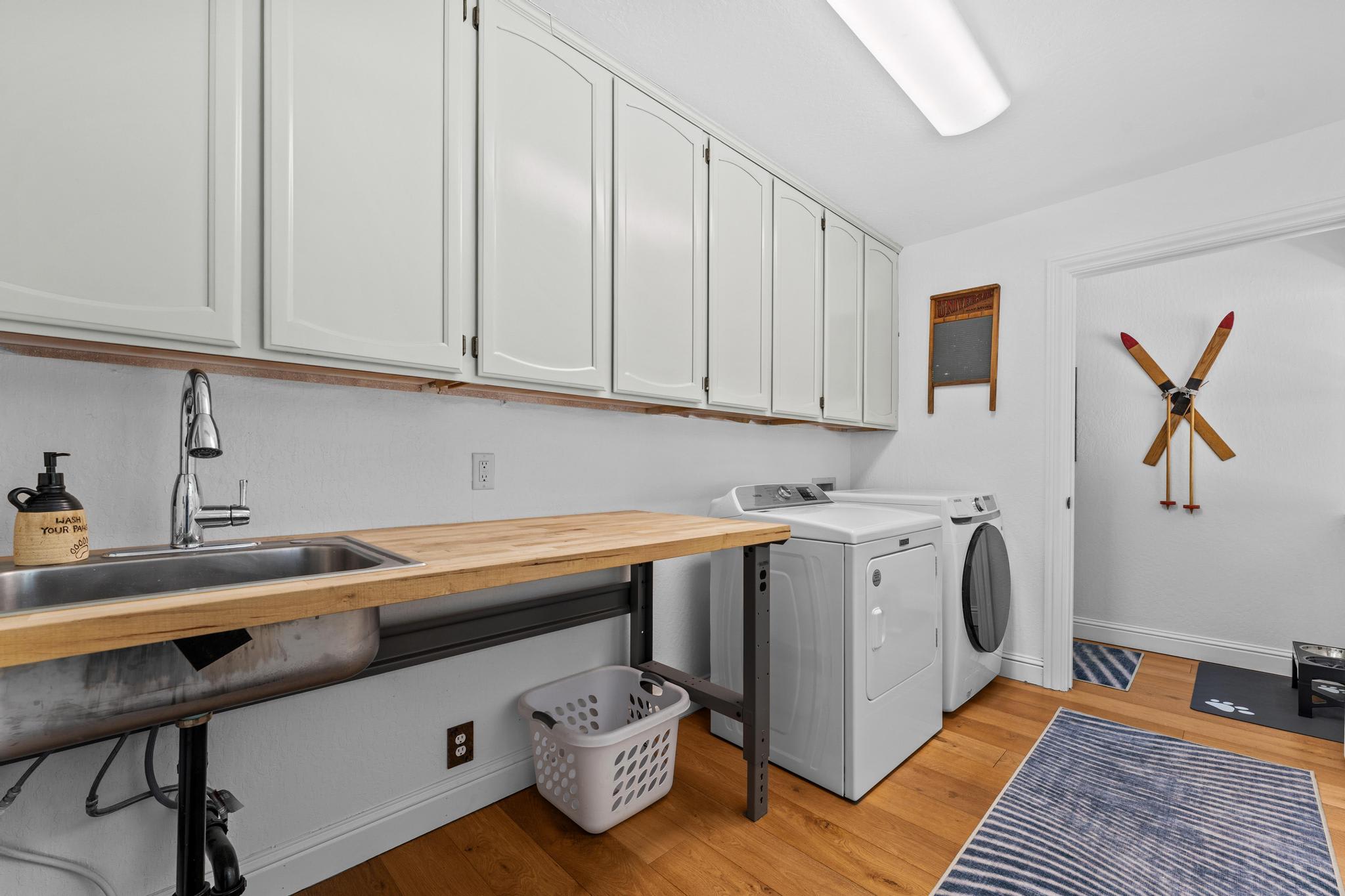 Laundry room in a Truckee vacation rental with washer, dryer, sink, ski decor, and blue rugs on wood floor.