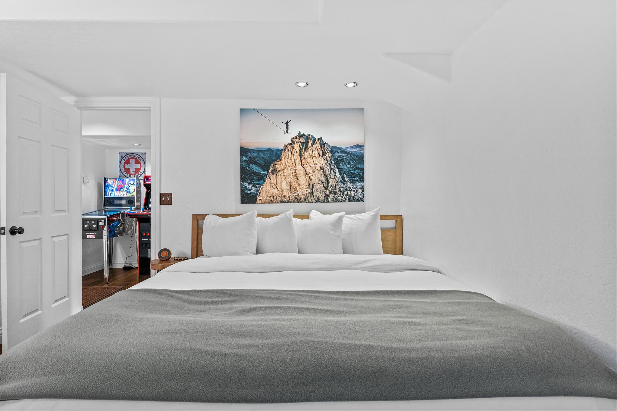 Cozy bedroom in a Truckee vacation rental with a large bed and pinball machine visible in the adjoining room.
