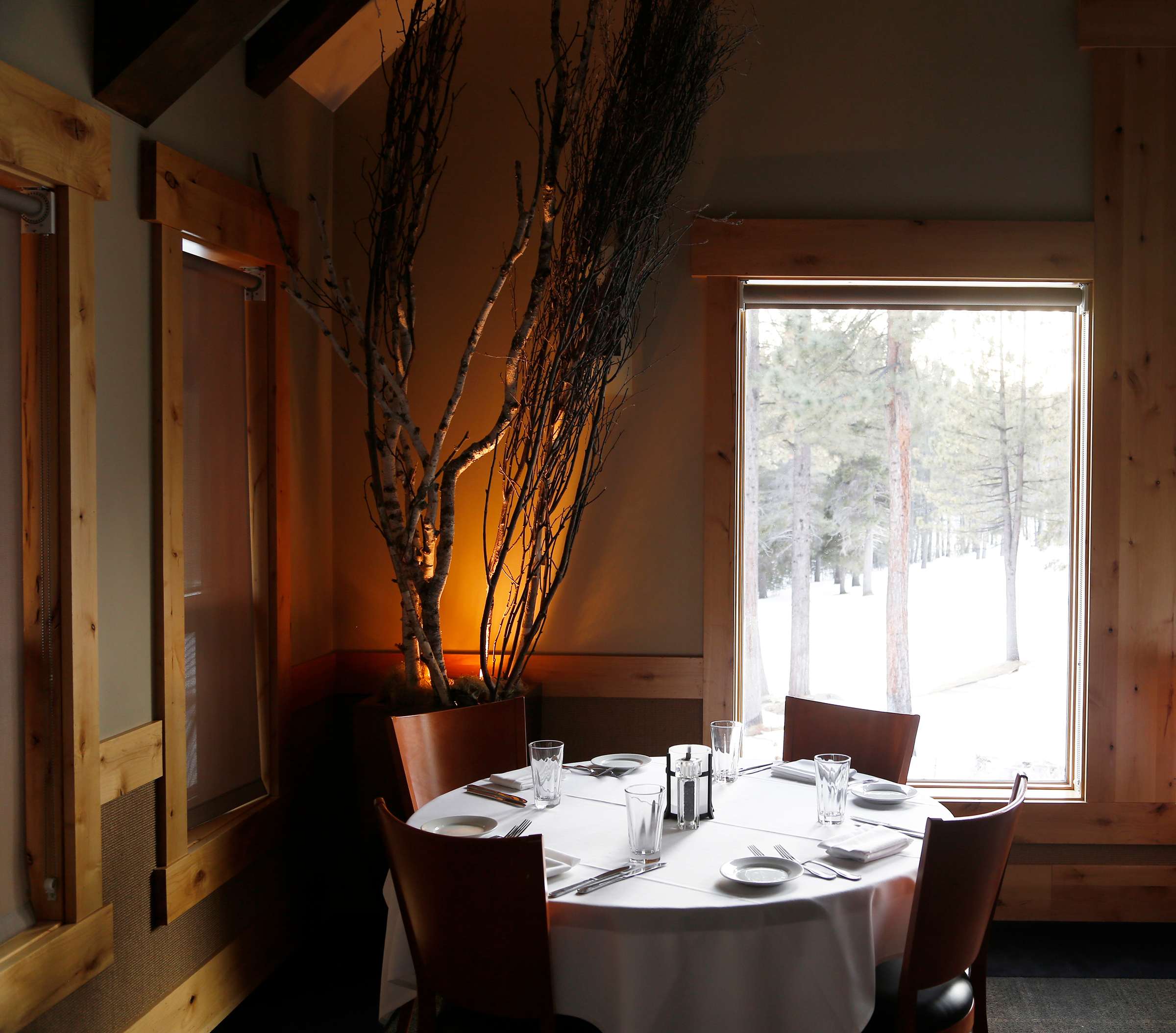 Cozy dining area in Truckee vacation rental with a window view of snowy pine trees, set for four with elegant decor.