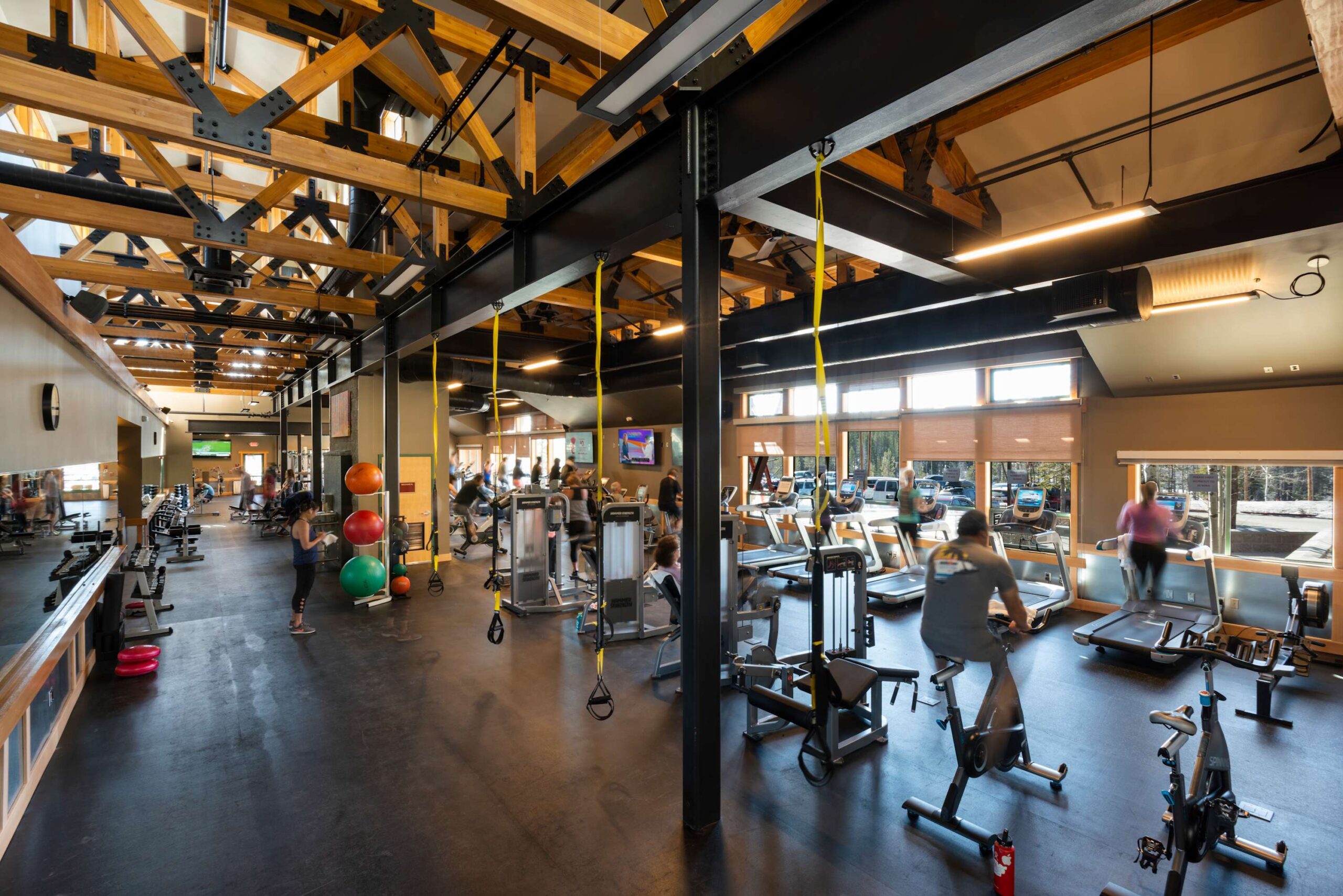People exercising in a modern gym at a Truckee vacation rental with exposed beams and large windows.