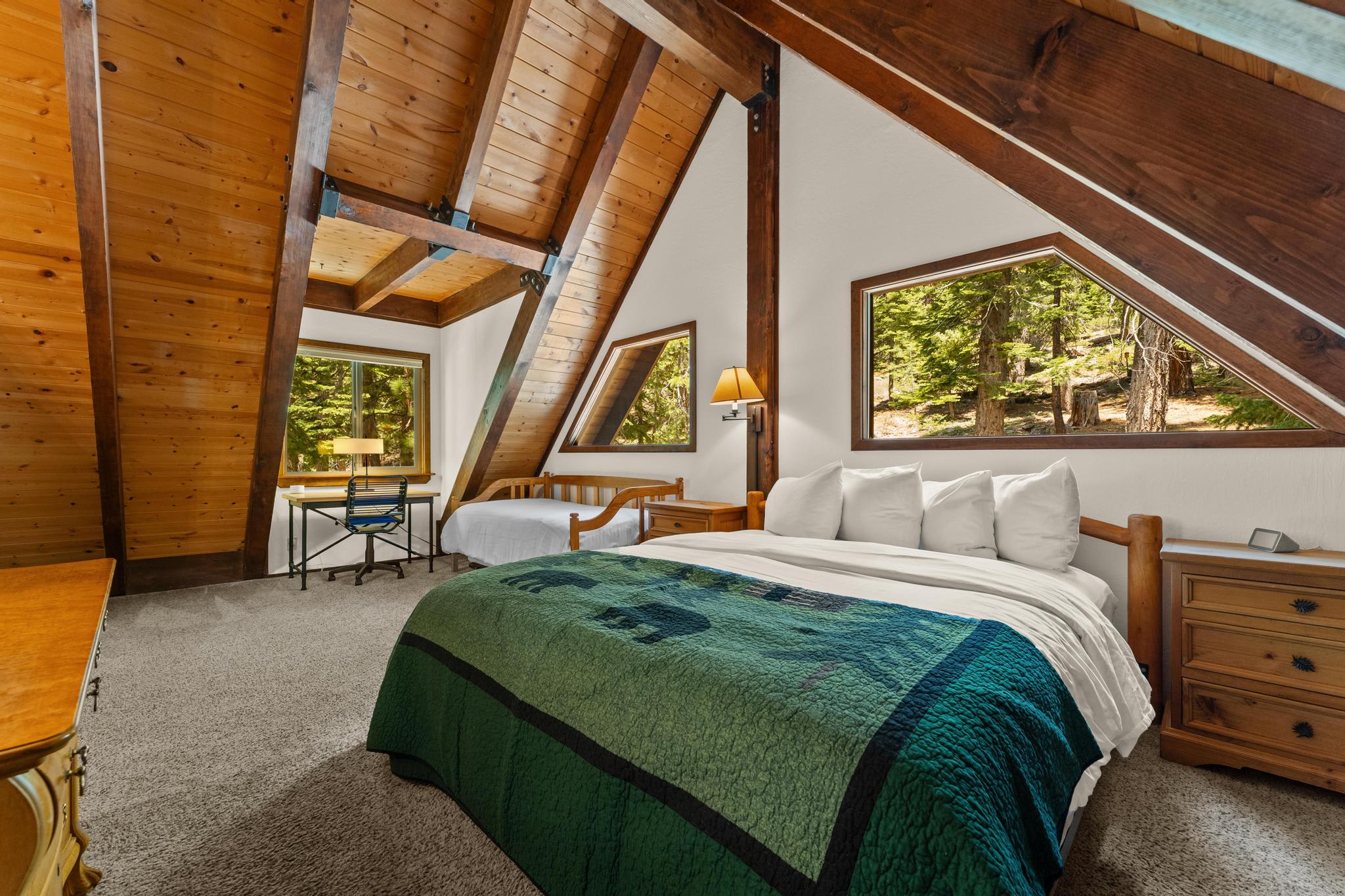 A-frame room in a Tahoe Vista vacation rental with wood beams, two beds, and forest view windows.