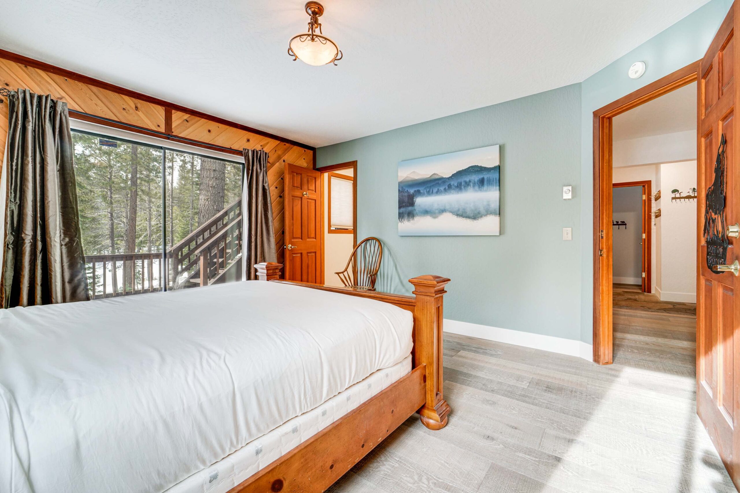Bedroom in Truckee vacation rental with wooden bed, landscape painting, and large window overlooking trees.