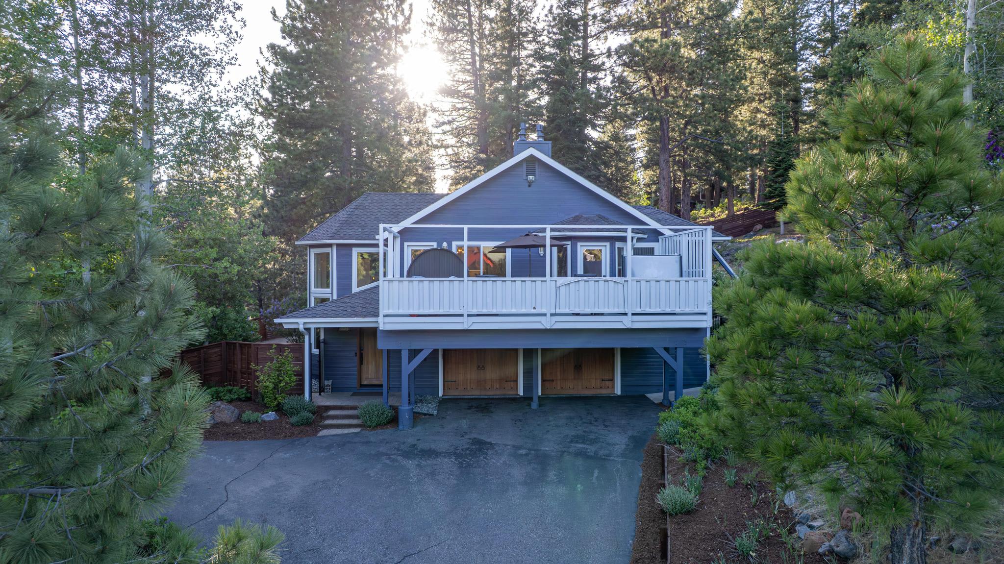 Charming Truckee vacation rental surrounded by tall pine trees with a spacious deck and a large driveway.