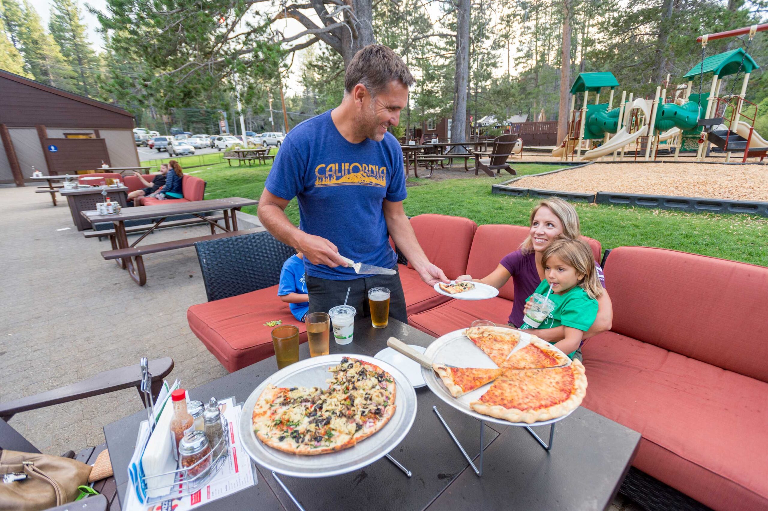 Family enjoys pizza outdoors at a Truckee vacation rental with playground and patio seating nearby.