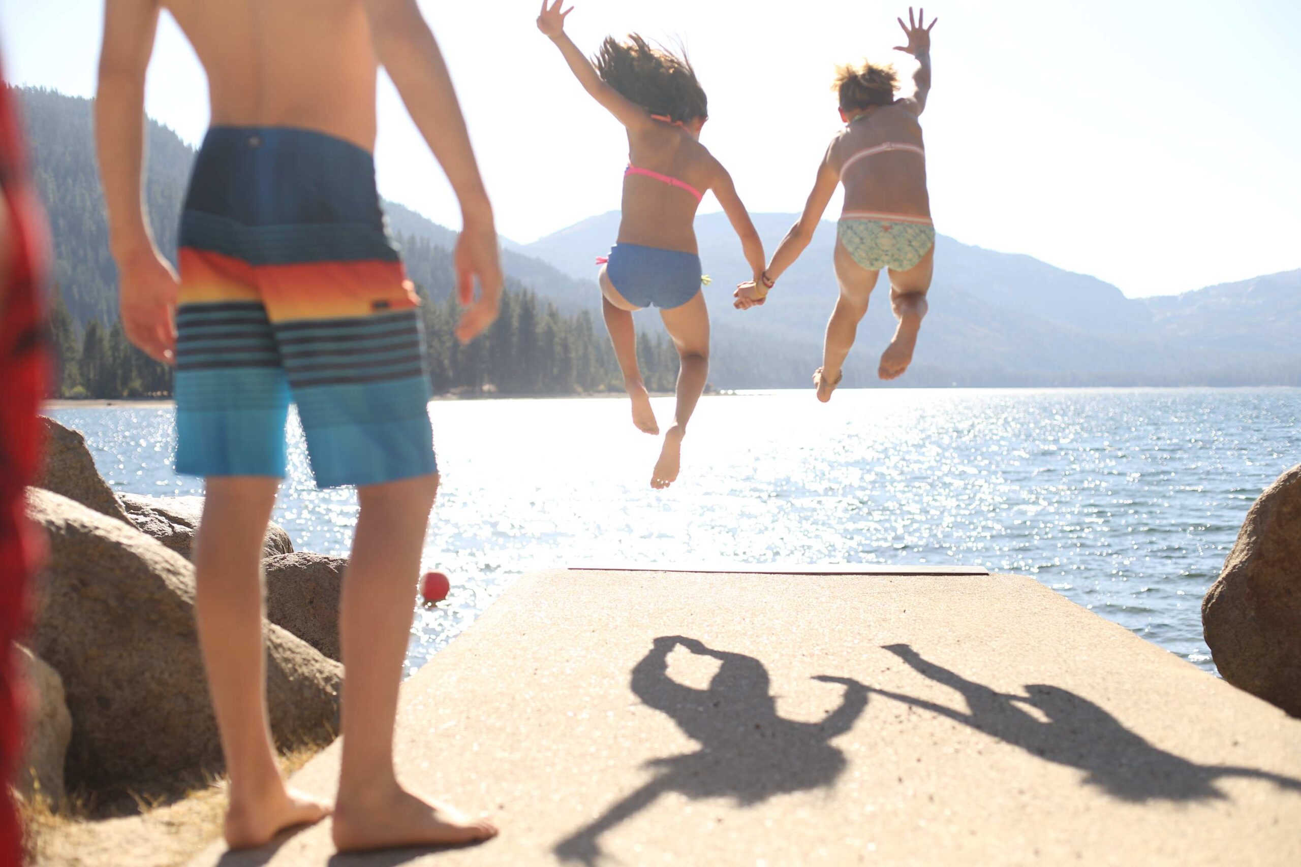 Kids jumping into a lake near a Truckee vacation rental, sunlight reflecting off the water and mountains in the background.