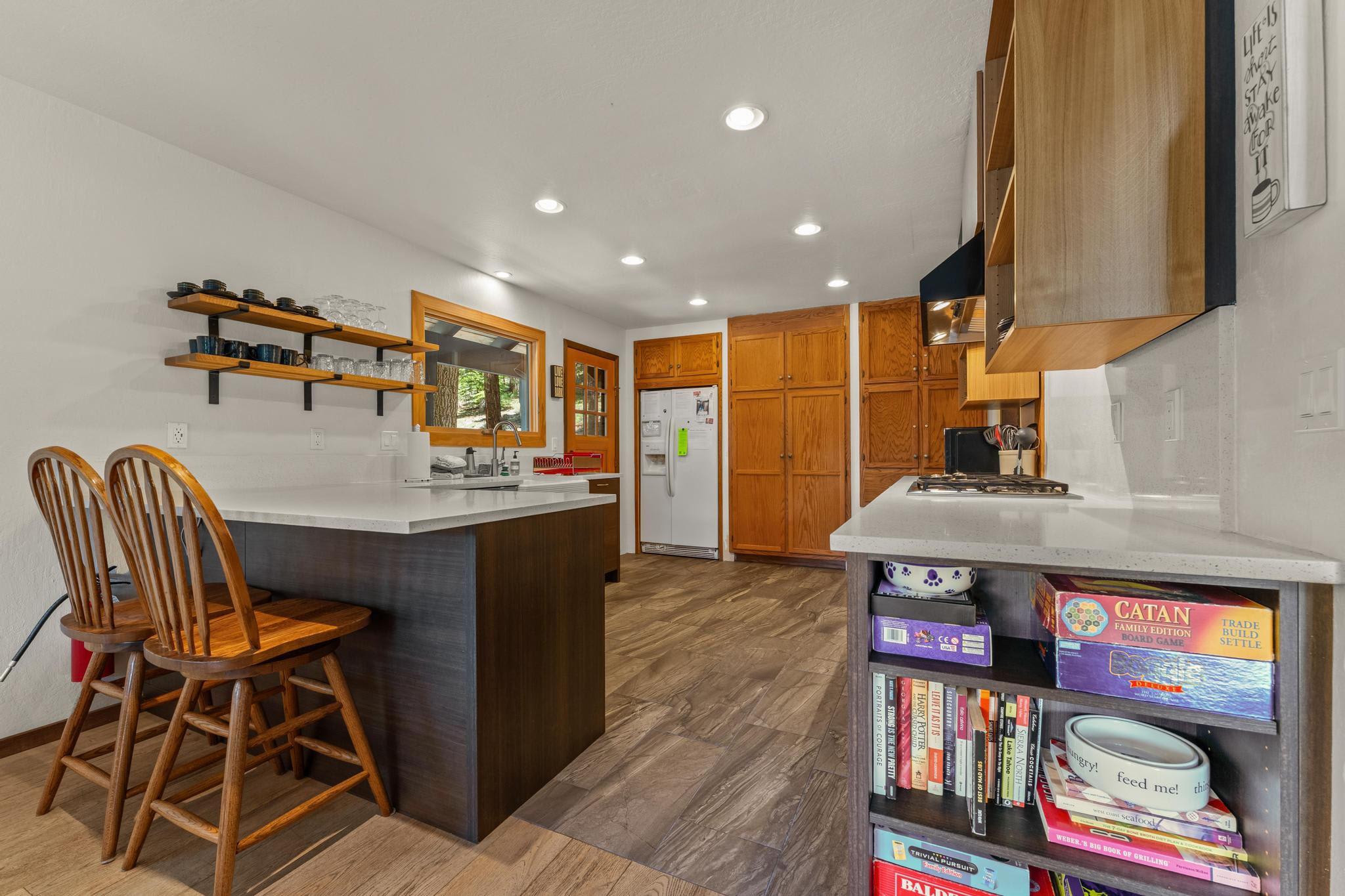 Modern kitchen in a Tahoe Vista vacation rental with wooden cabinets, bar stools, and shelves displaying dishes.
