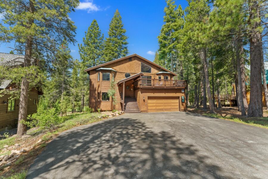 Wood cabin-style vacation rental surrounded by trees in Truckee, featuring a spacious driveway and sunny exterior.