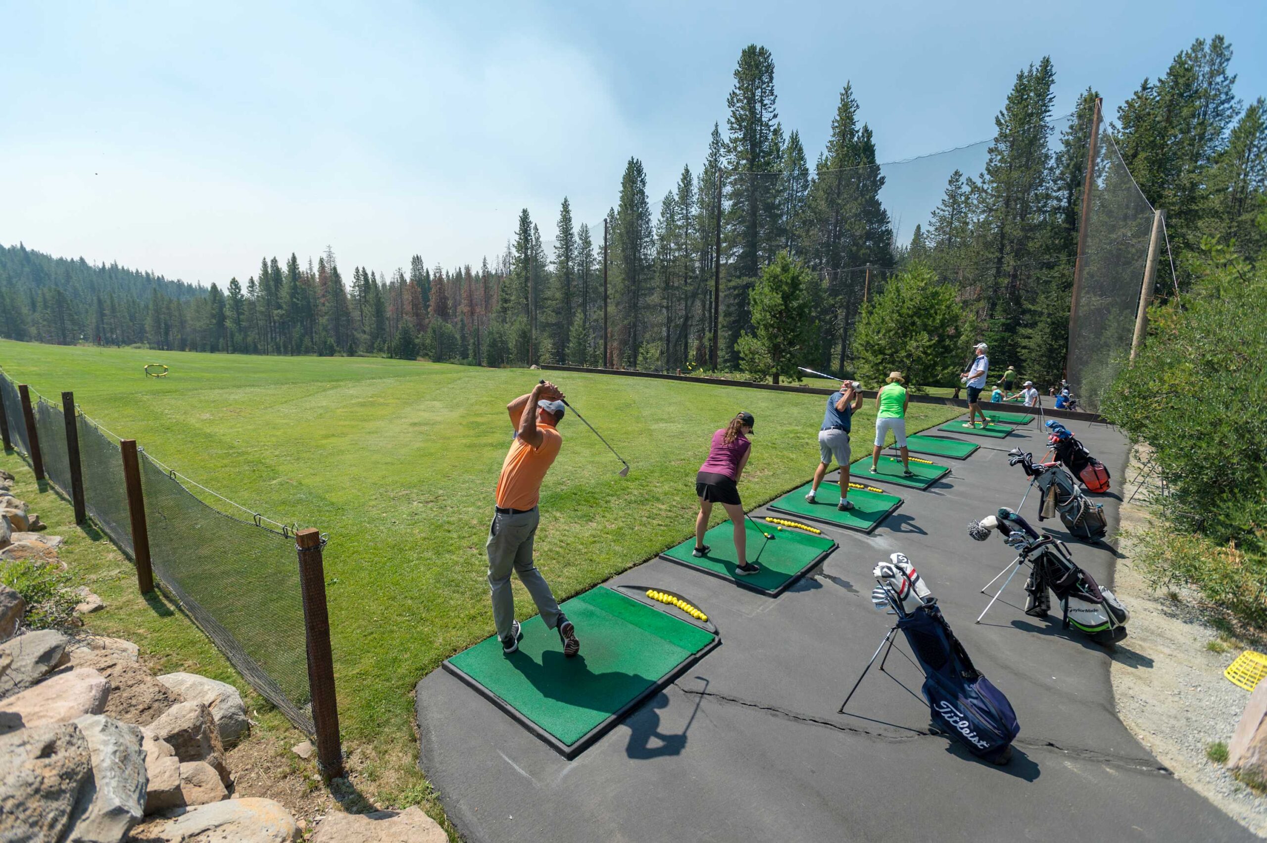 Golfers practicing at a driving range near a forest, perfect for a Truckee vacation rental experience.