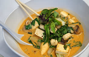 Bowl of curry with tofu and greens at a Truckee vacation rental, garnished with basil and cashews, served with chopsticks.
