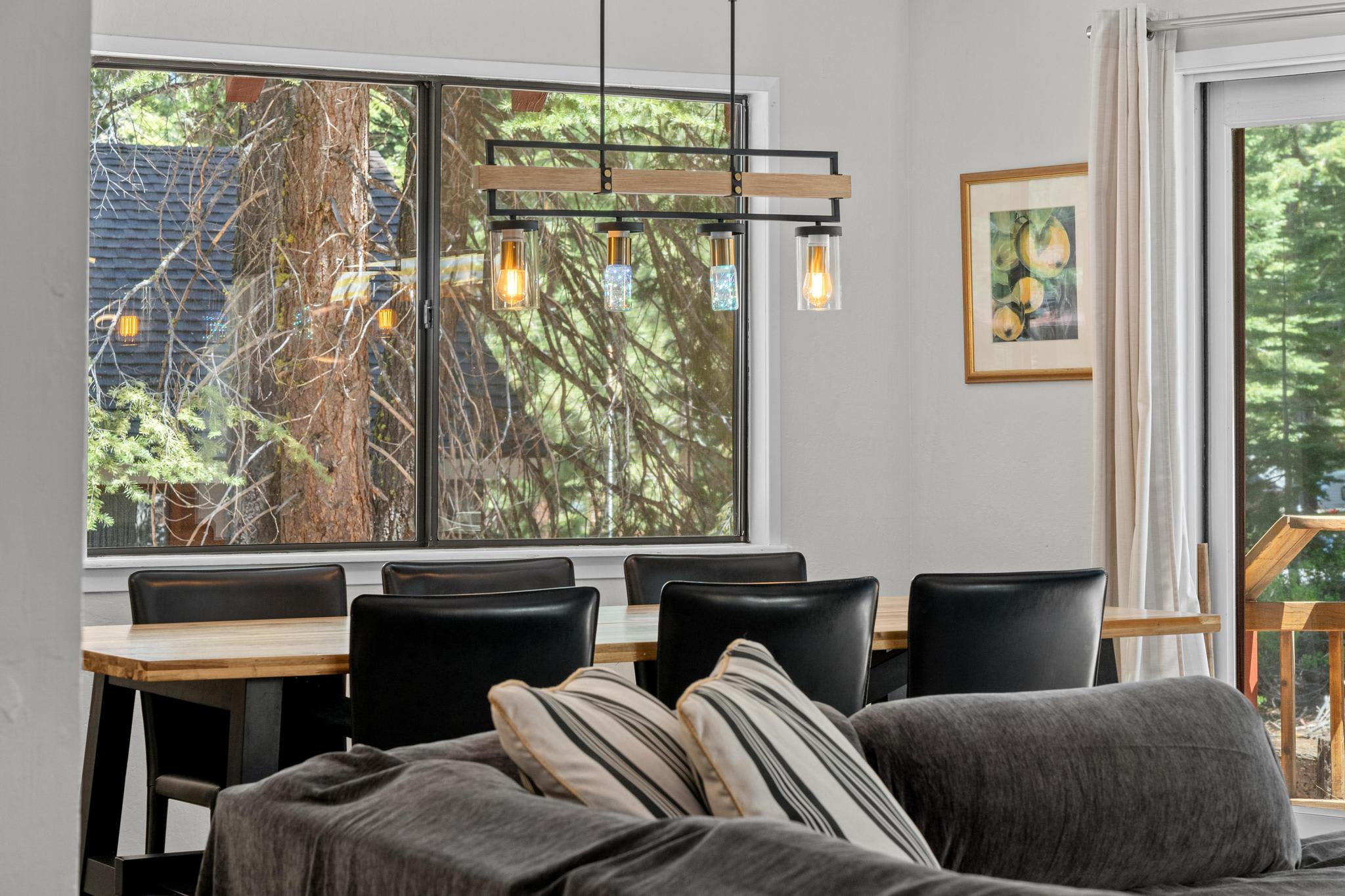 Dining area in Tahoe Vista vacation rental with a view of trees through large windows and modern lighting.