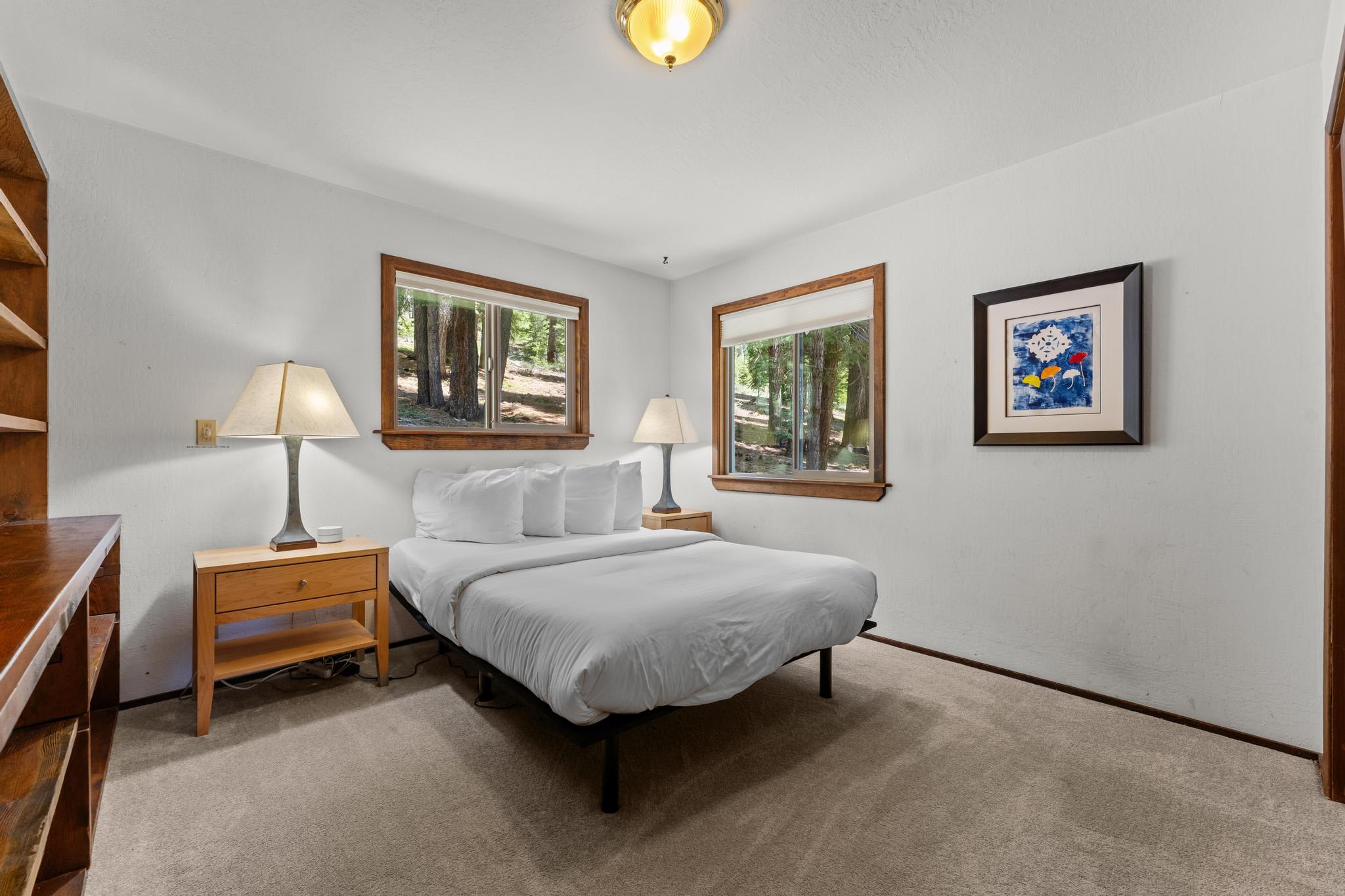 Cozy bedroom in Tahoe Vista vacation rental, featuring a bed, framed art, and forest views through large windows.