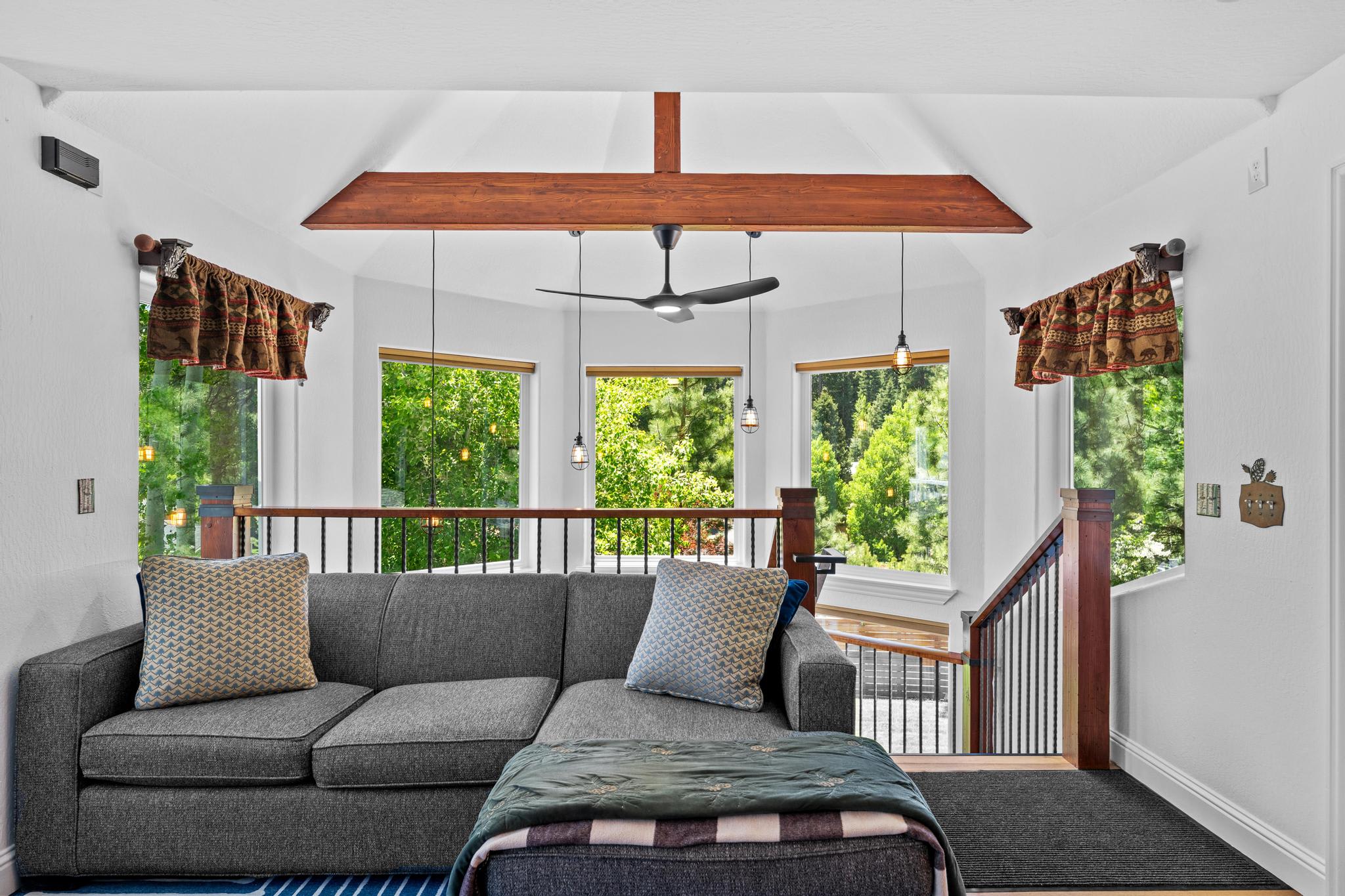 Cozy living room in a Truckee vacation rental, featuring a grey sofa, exposed beams, and large windows with forest views.