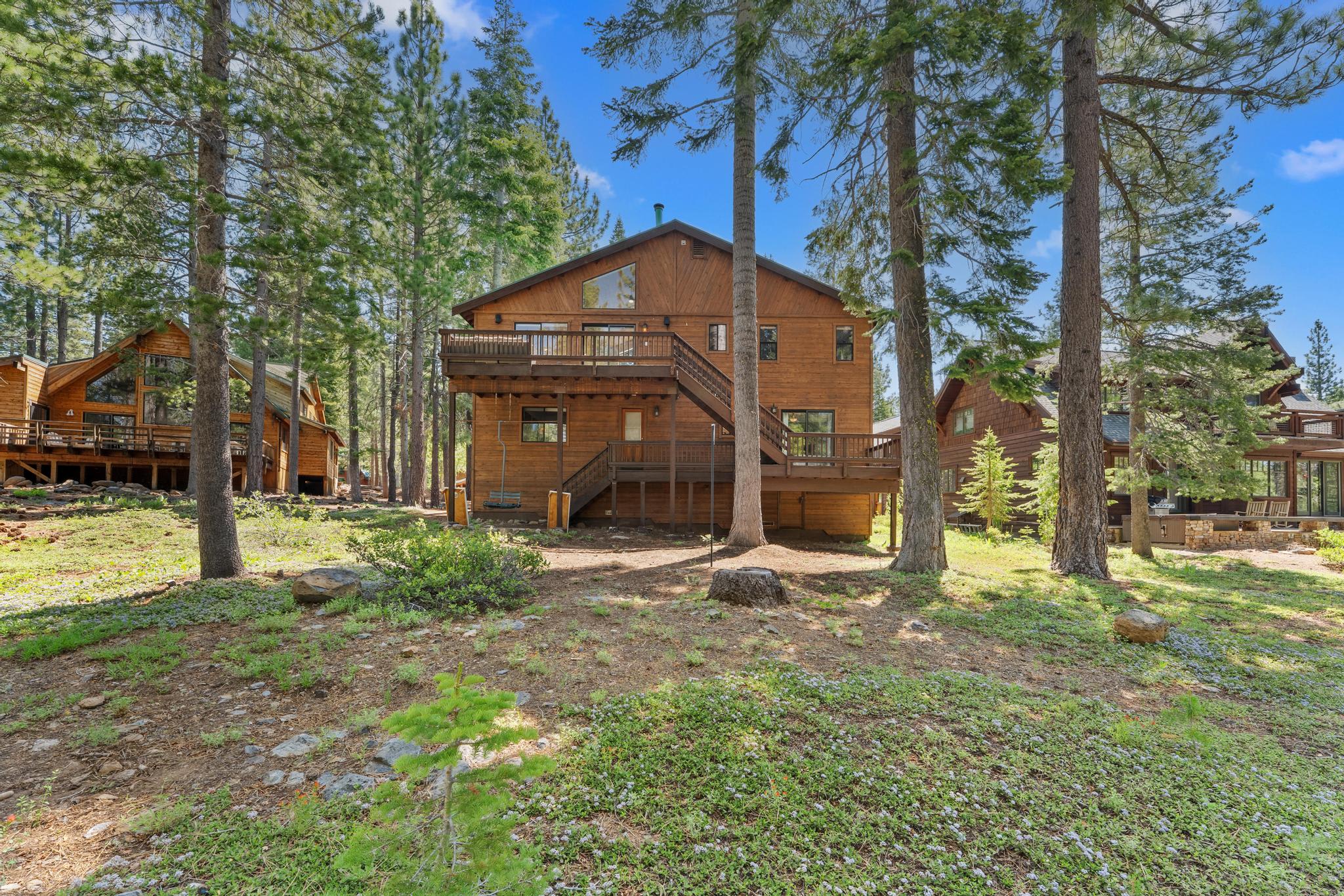 Rustic wooden vacation rental in Truckee, nestled among tall pine trees, under a clear blue sky.
