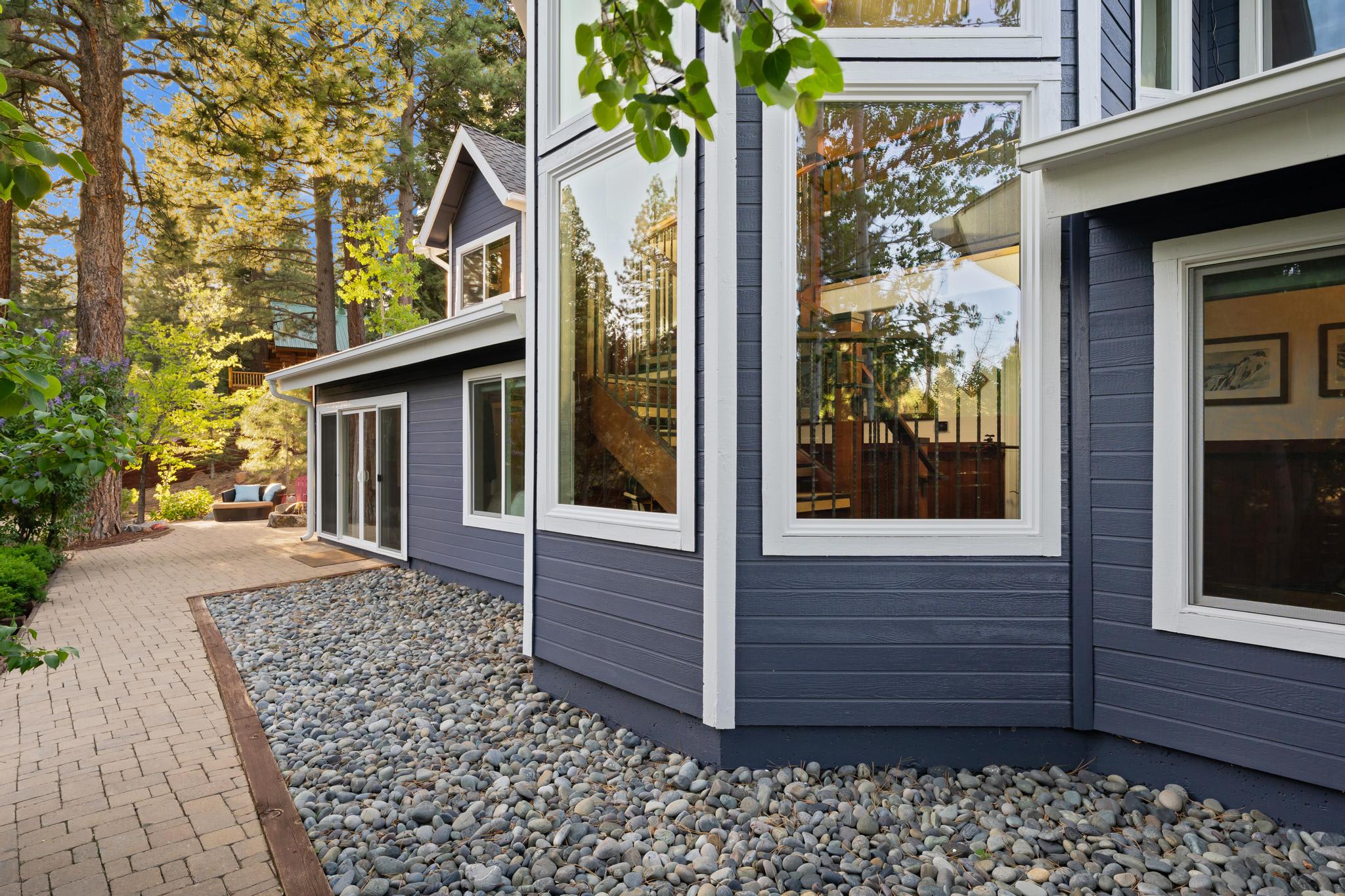 Modern Truckee vacation rental with large windows, nestled in a wooded area with a stone path and lush greenery.