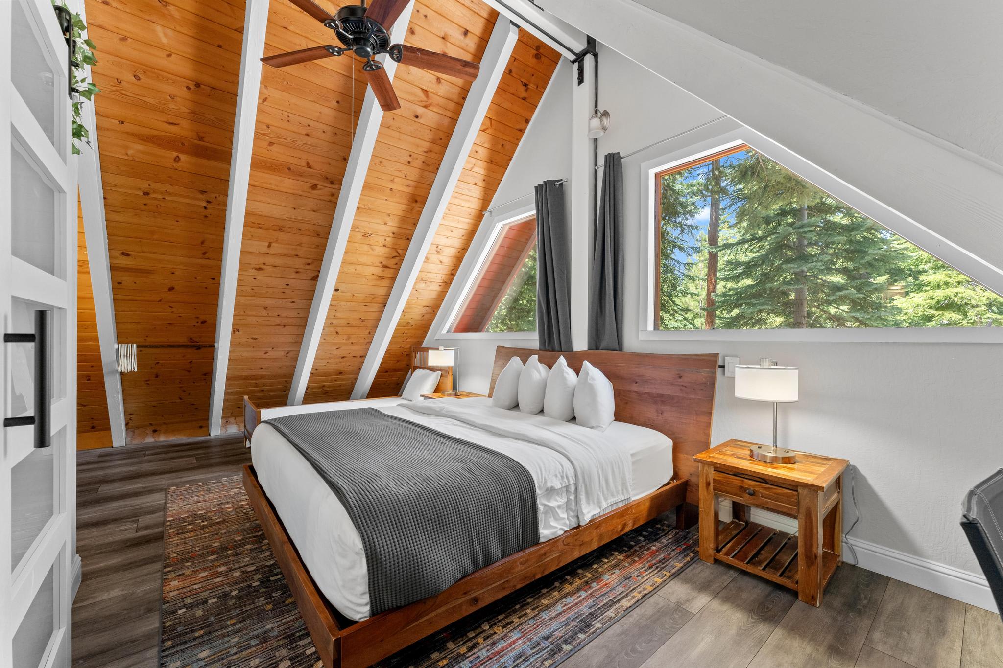 Cozy attic bedroom in a Tahoe Vista vacation rental with wooden ceiling, large windows, and forest views.