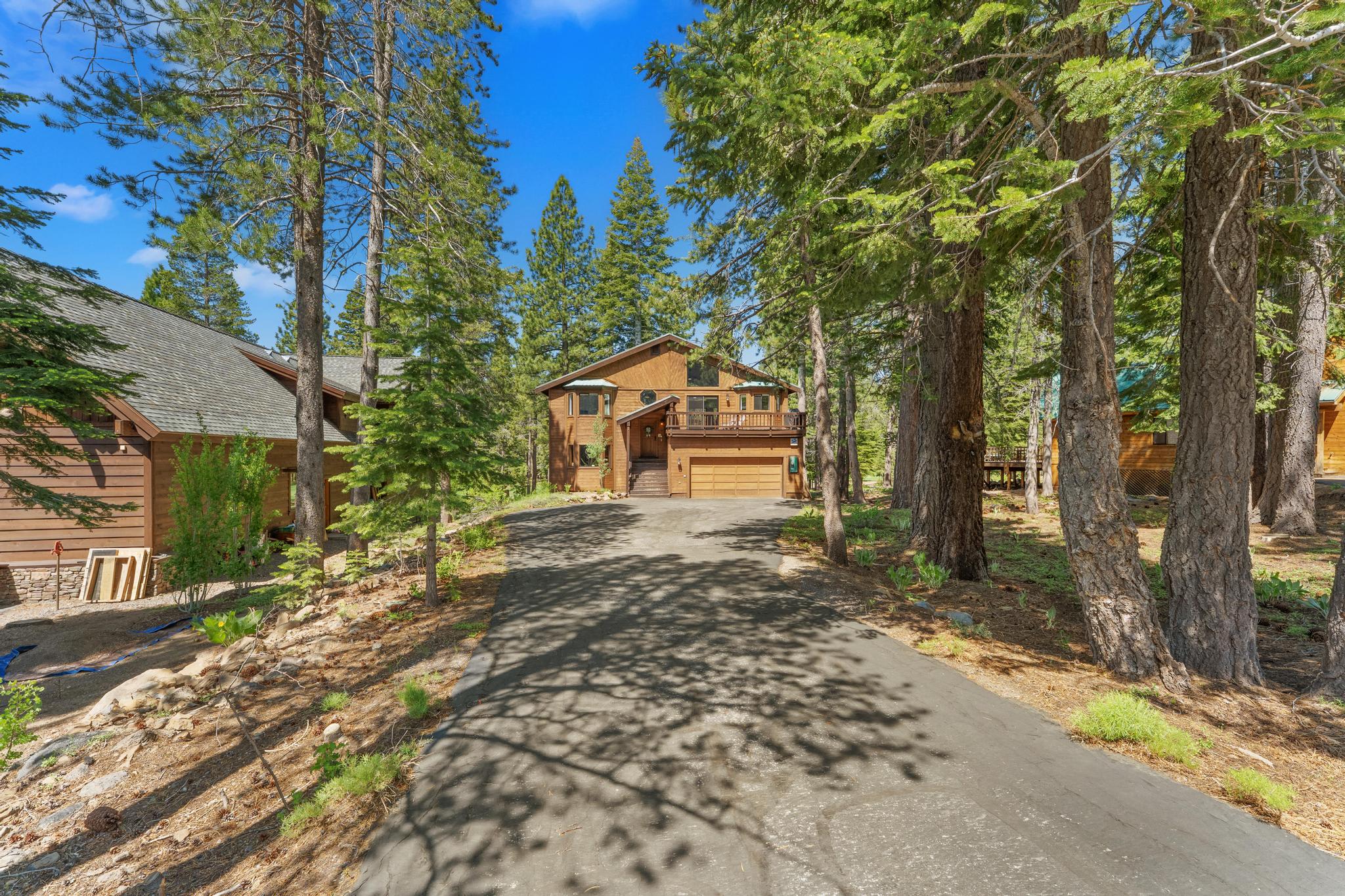 A cozy wood cabin surrounded by trees serves as a vacation rental in Truckee, featuring a driveway and deck.