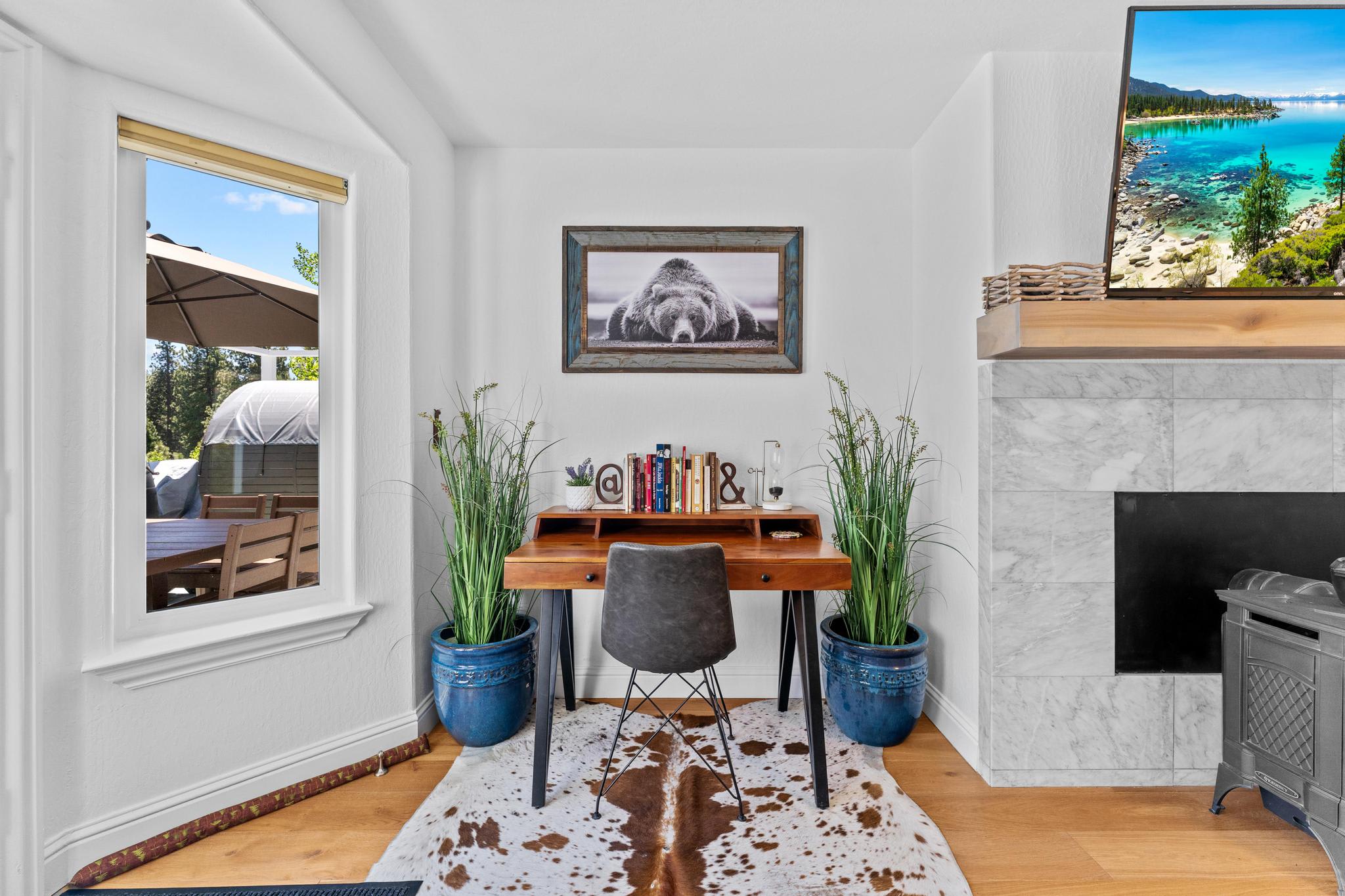 Cozy workspace in a Truckee vacation rental with framed bear photo, desk, plants, cowhide rug, and outdoor view.