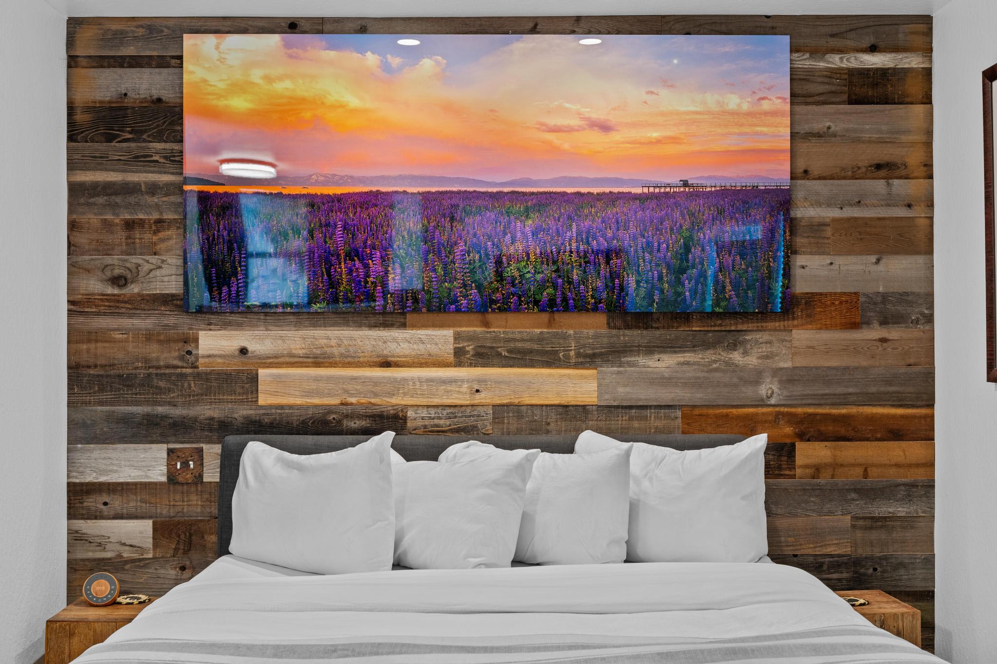 Cozy bedroom at a Truckee vacation rental with rustic wooden wall and vibrant landscape art above the bed.