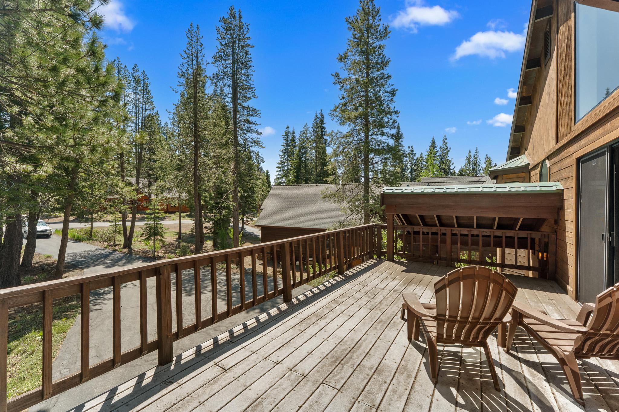 Deck view from a Truckee vacation rental, showing Adirondack chairs and surrounding pine trees under a clear blue sky.