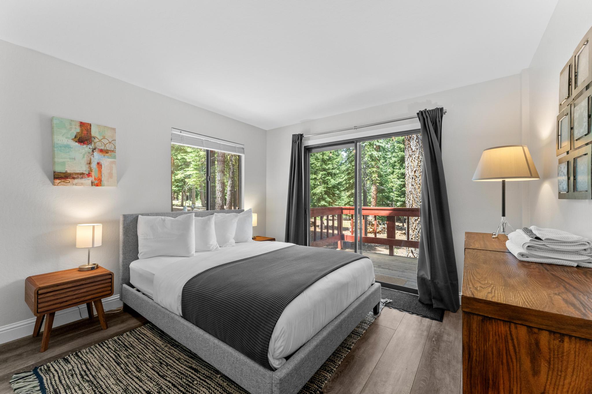 Bright bedroom in a Tahoe Vista vacation rental with modern decor, large windows, and forest views from the balcony.