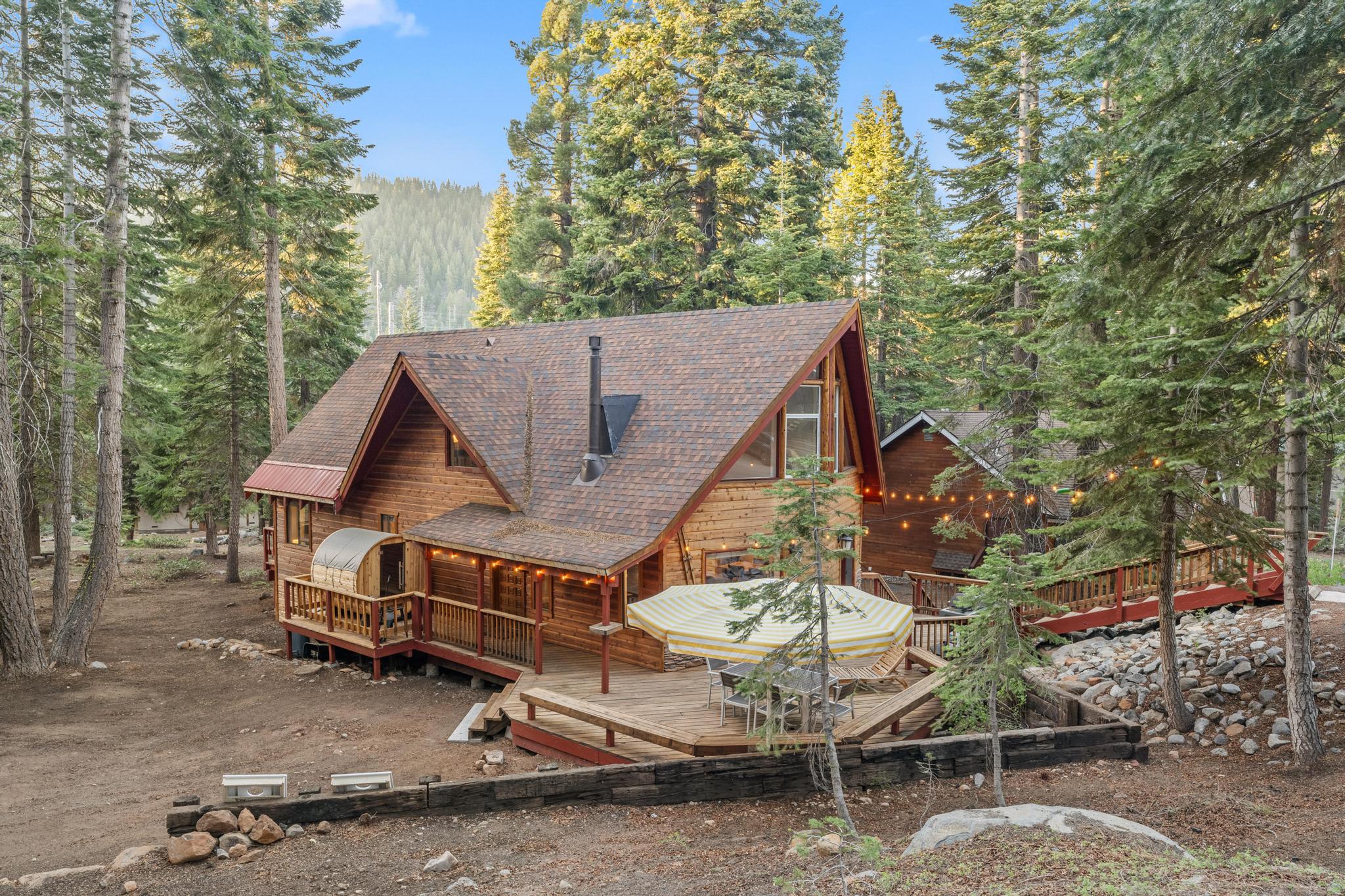 Charming cabin-style vacation rental in Tahoe Vista, nestled among tall trees with a spacious wooden deck and string lights.