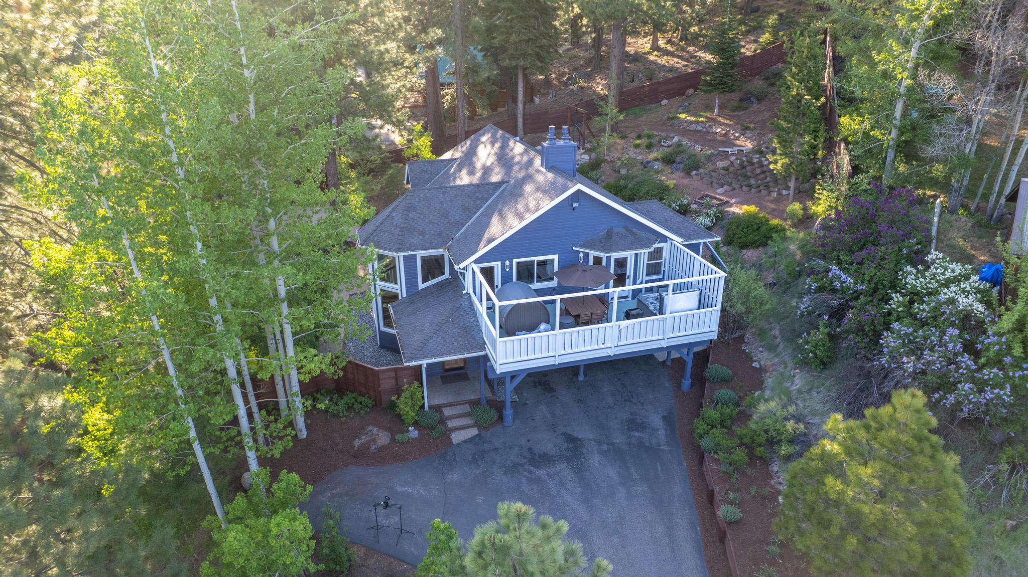 Aerial view of a charming blue vacation rental surrounded by lush trees in Truckee, featuring a spacious deck.