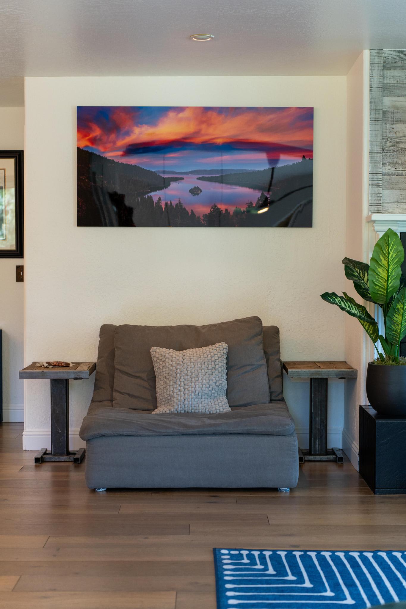 Cozy Truckee vacation rental interior with a gray chair, vibrant landscape art, wooden side tables, and a green plant.