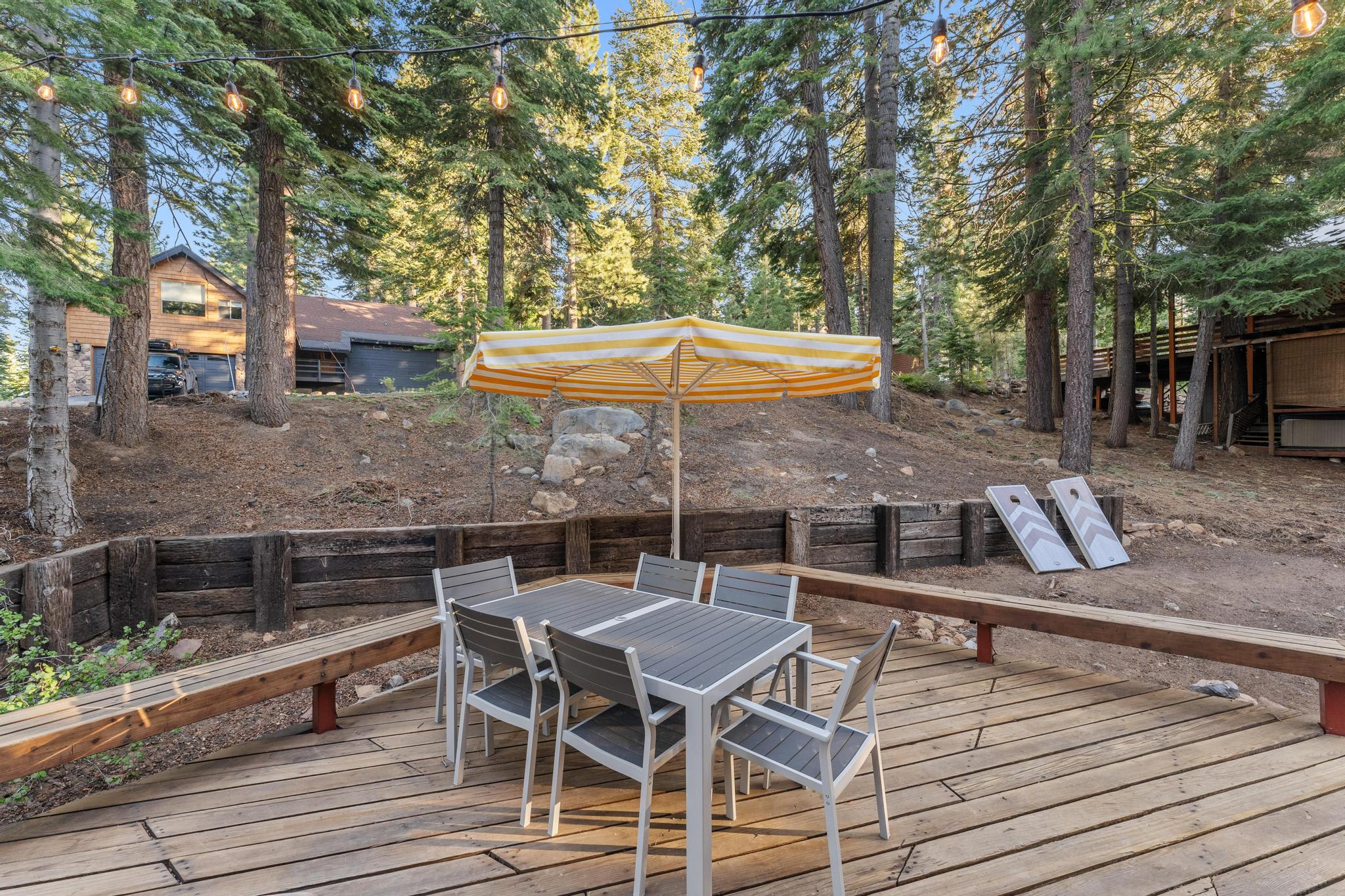 Outdoor deck with dining set and umbrella at a vacation rental in Tahoe Vista, surrounded by trees and festive lights.