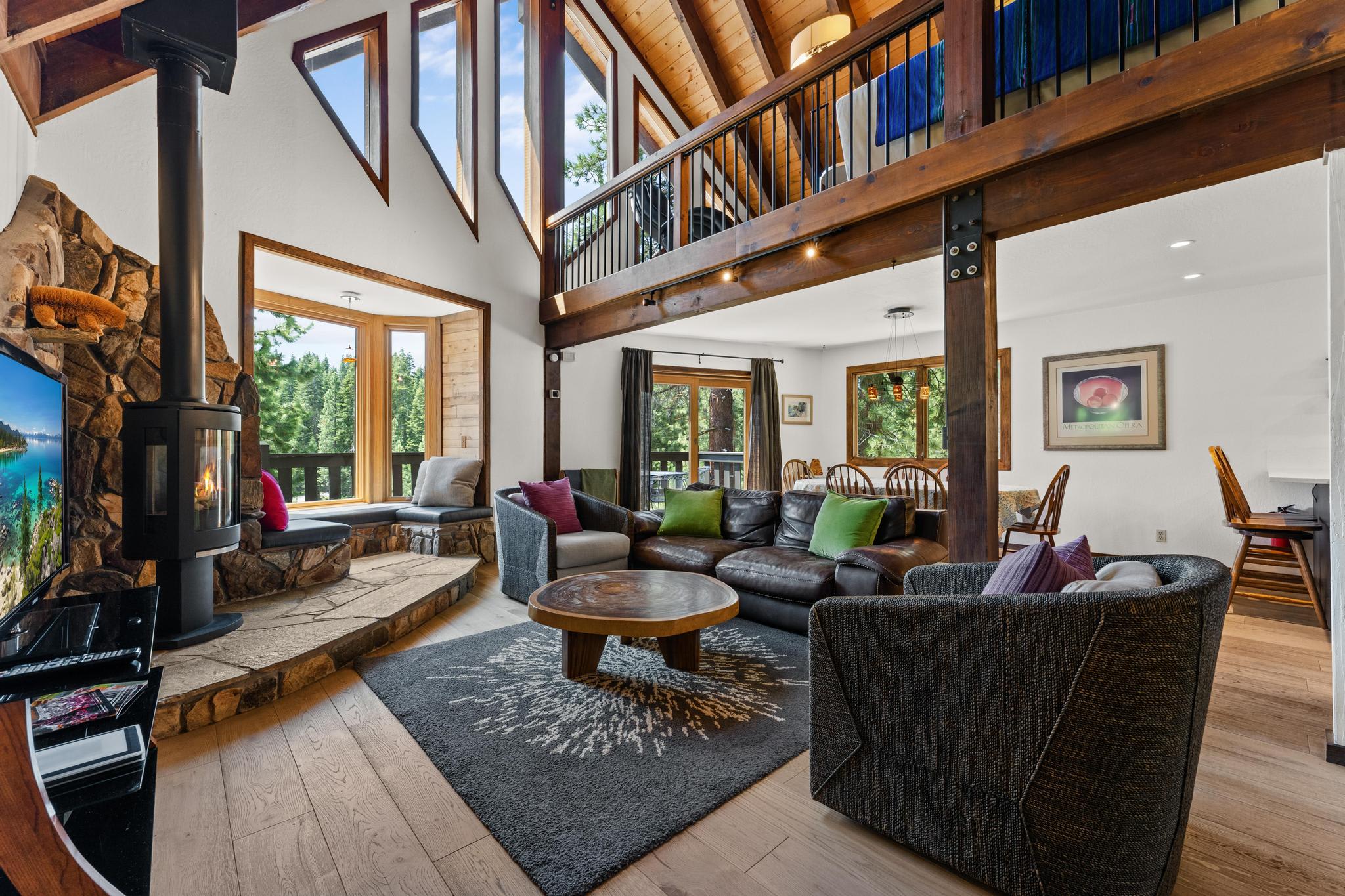 Cozy Tahoe Vista vacation rental living room with high ceilings, large windows, and a rustic fireplace.