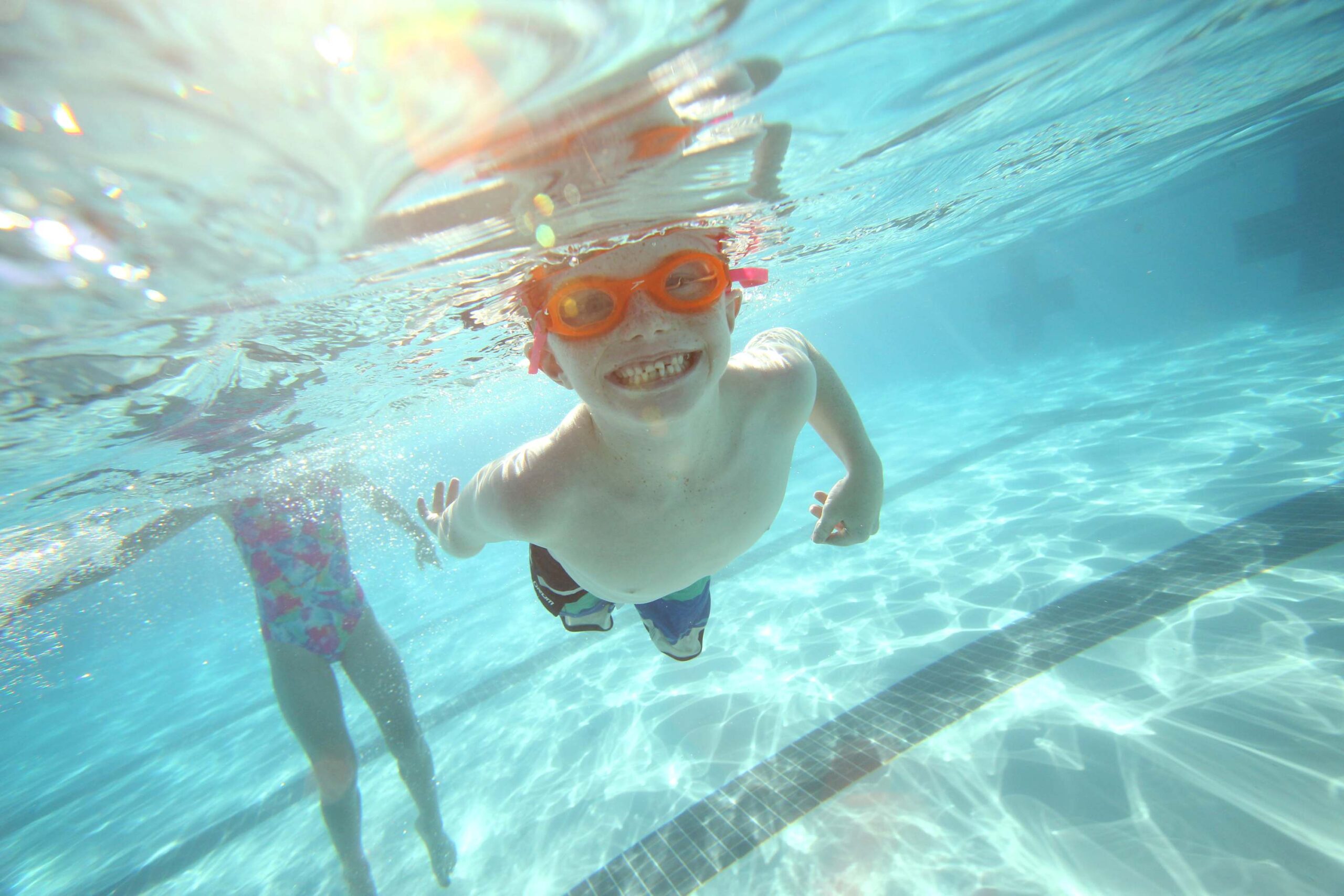 Child swimming underwater in a pool with goggles at a Truckee vacation rental, smiling and enjoying the clear blue water.