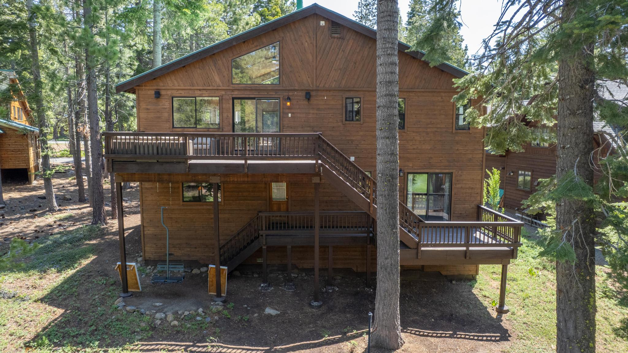 Spacious wood cabin-style vacation rental in Truckee, surrounded by tall trees with a large outdoor deck and stairs.