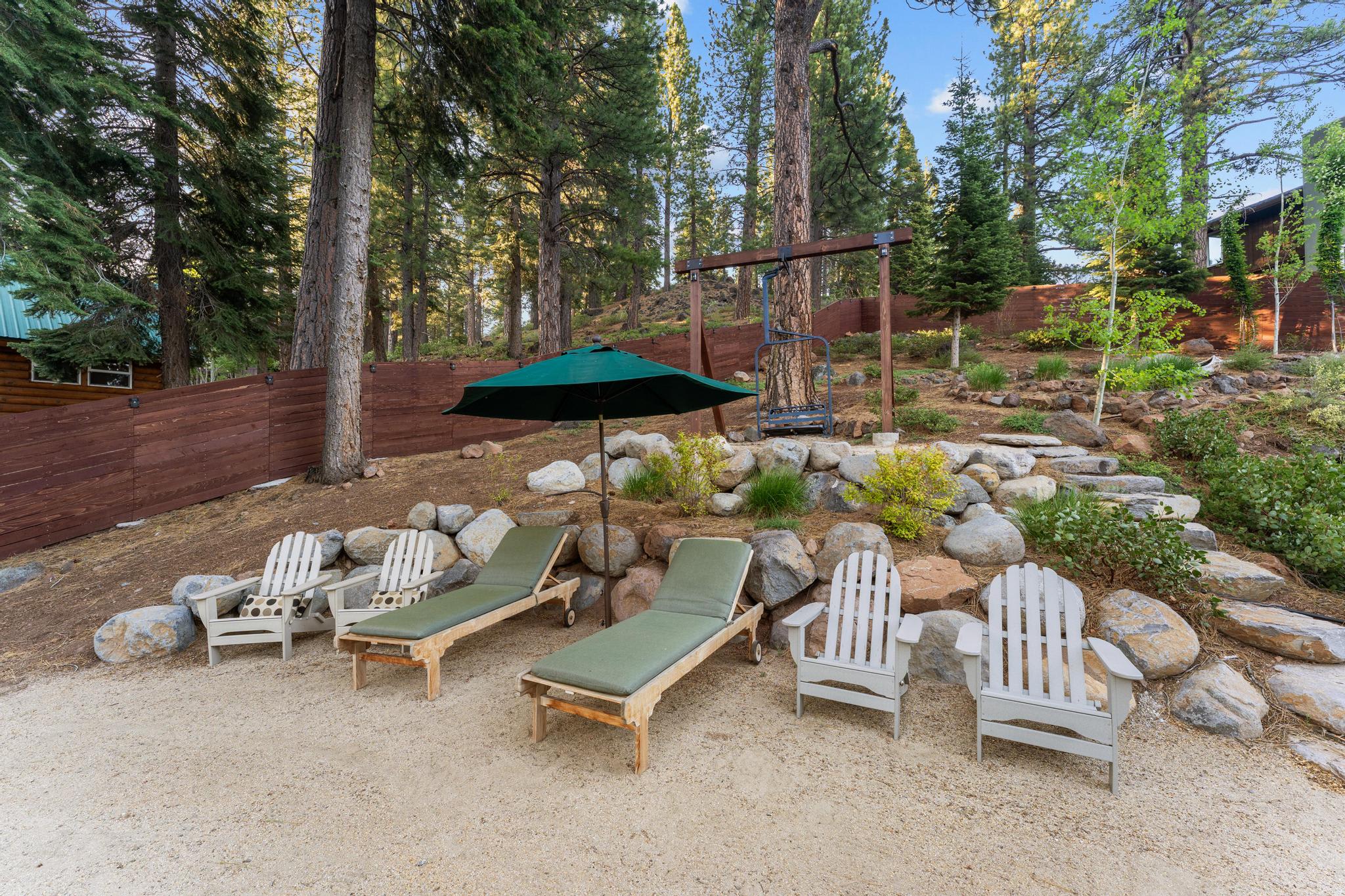 Outdoor patio with Adirondack chairs and loungers at a Truckee vacation rental, surrounded by trees and rocks.