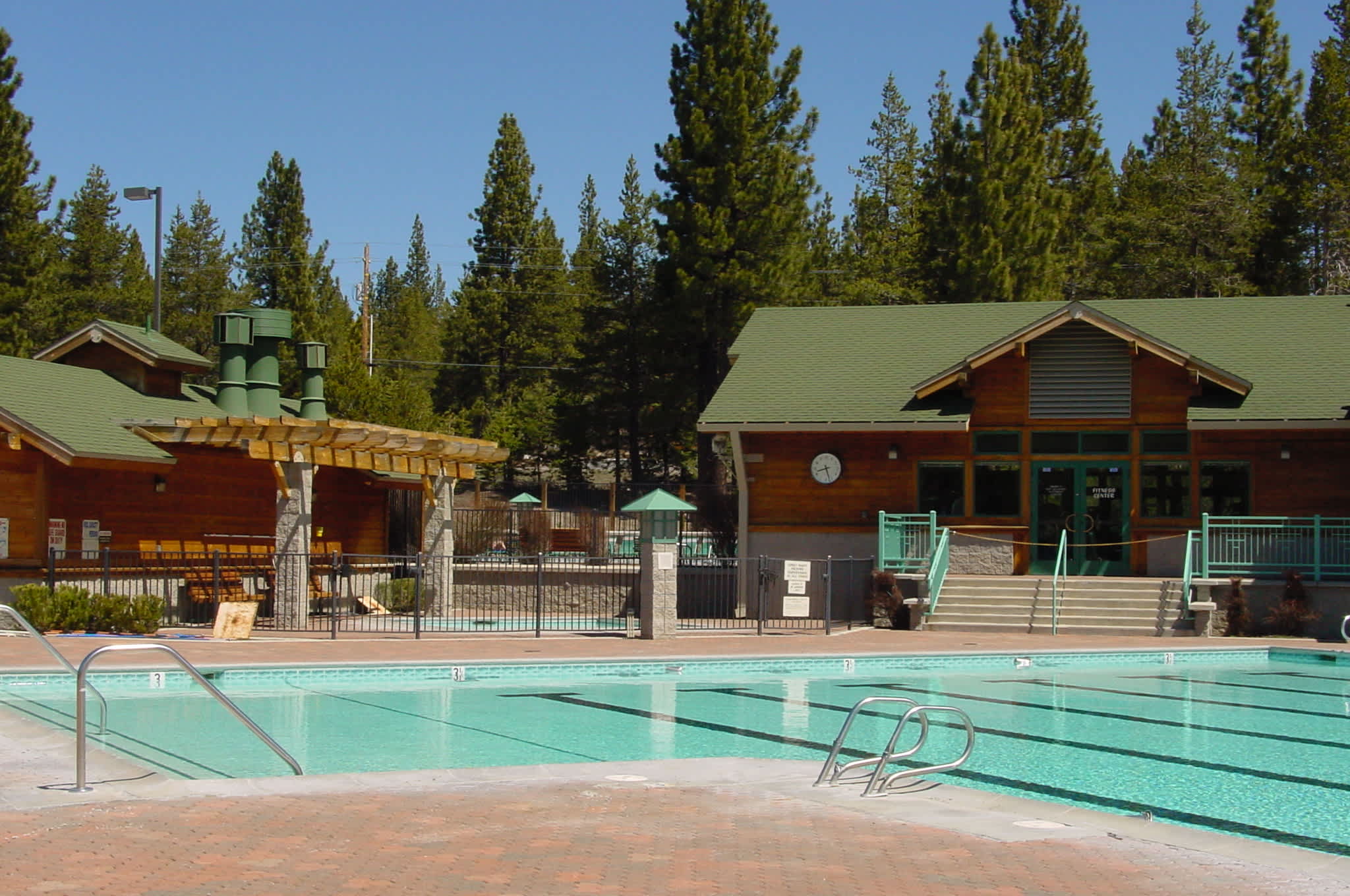 Outdoor pool at a Truckee vacation rental, surrounded by trees and a rustic lodge building under a clear blue sky.