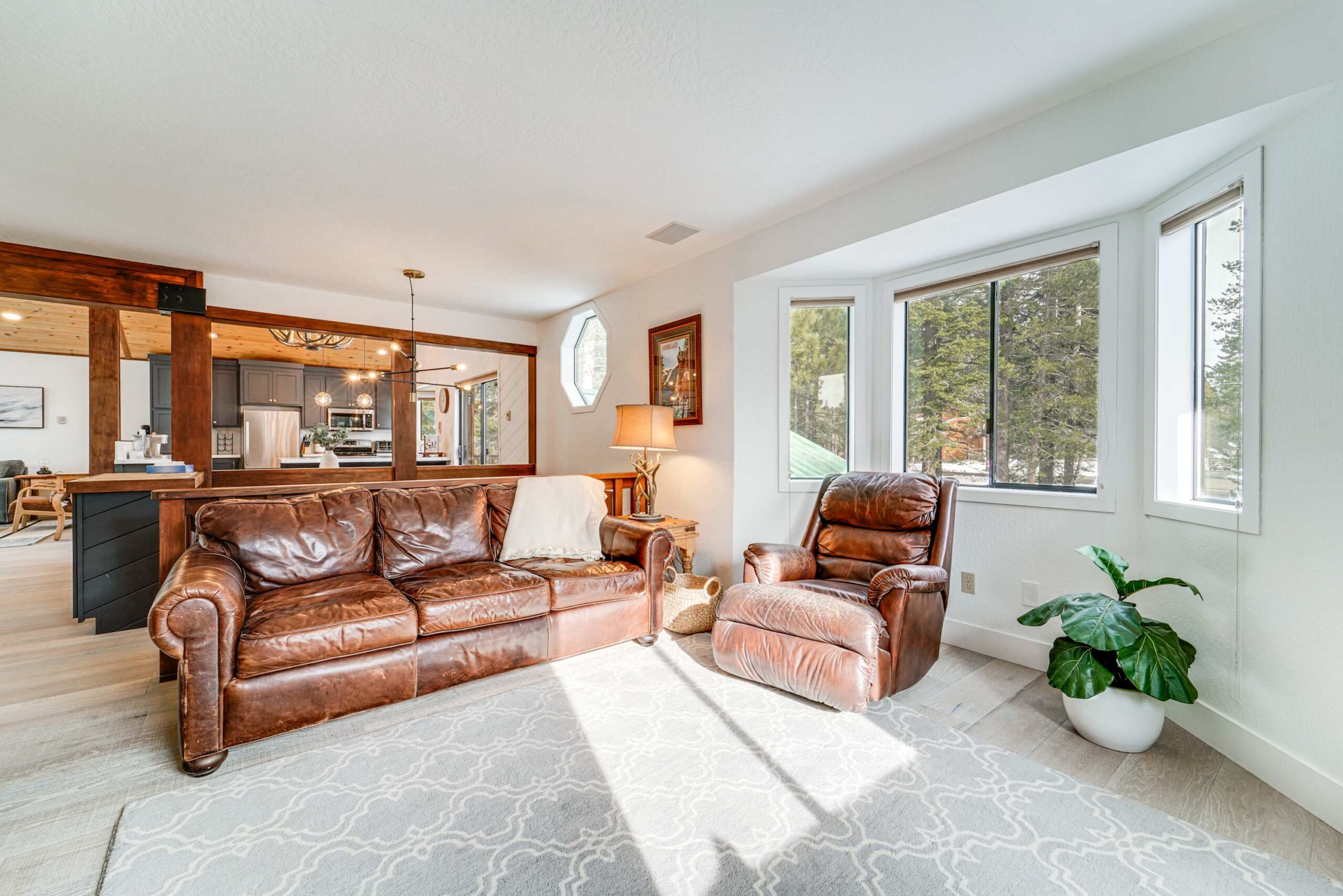 Cozy living area in a Truckee vacation rental, featuring leather seating, large windows, and a view of lush trees.