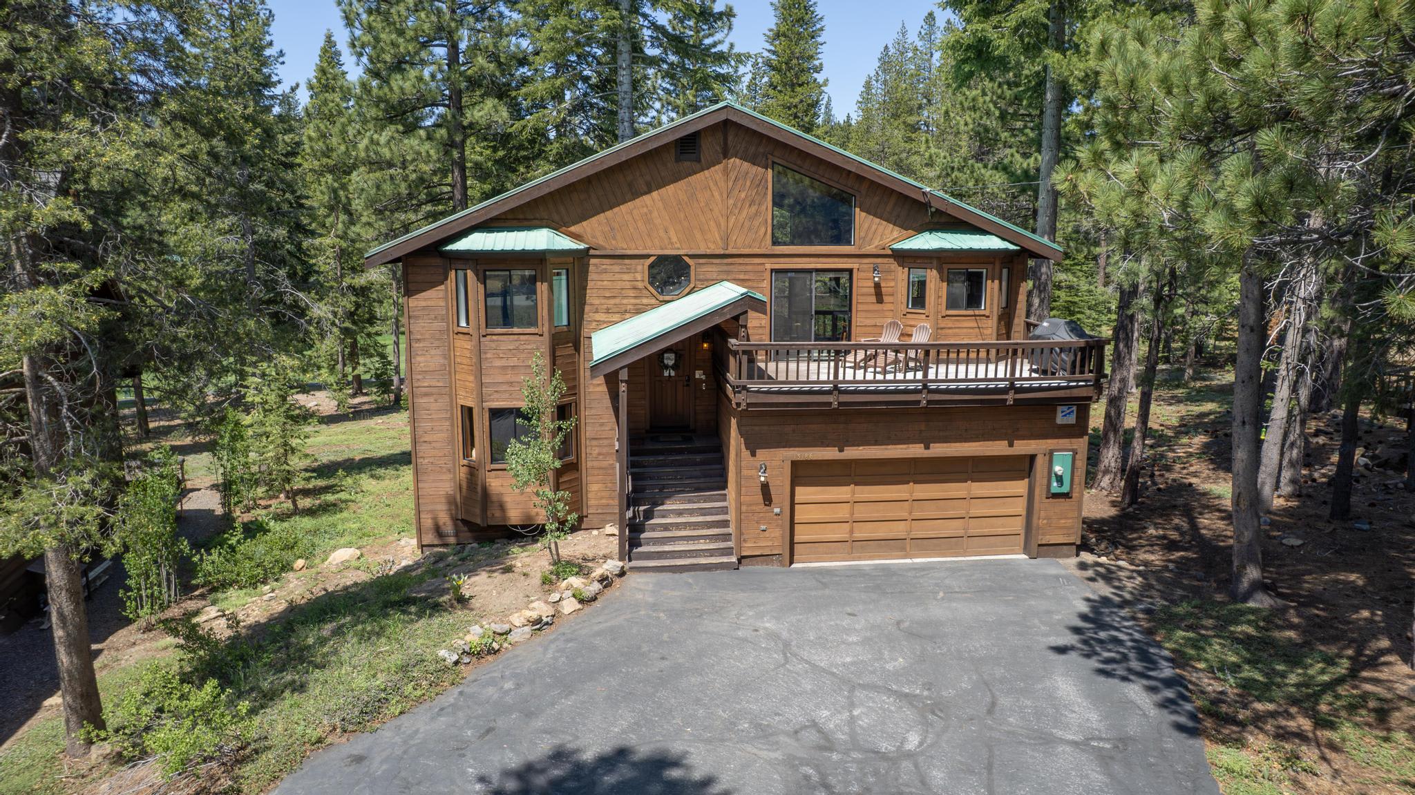 Wooden cabin-style vacation rental in Truckee, nestled among tall pine trees with a spacious driveway and deck.