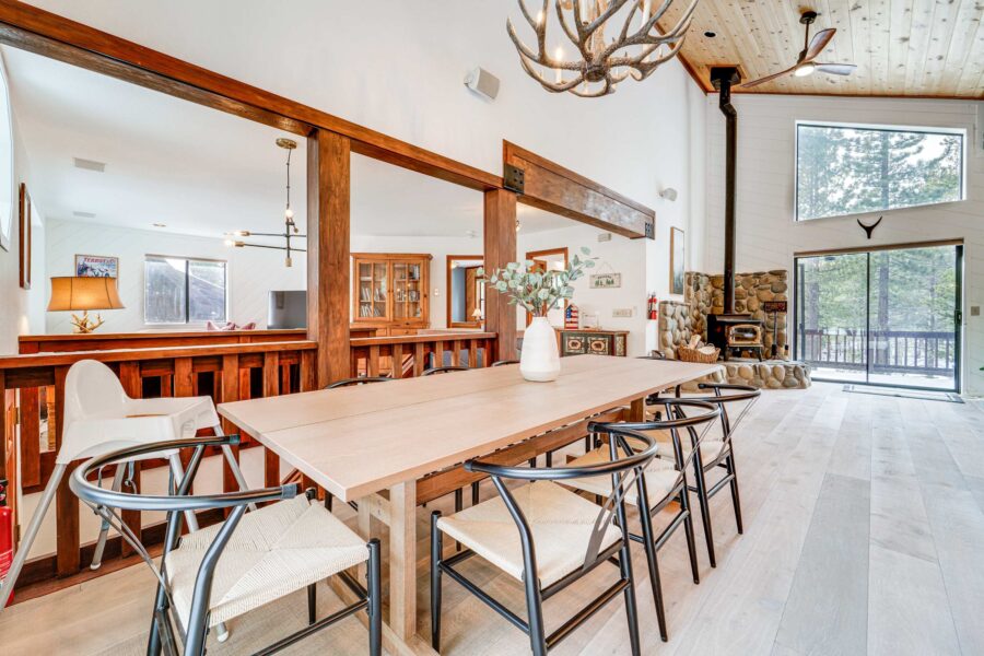 Spacious dining area in a Truckee vacation rental with wooden elements, antler chandelier, and a stone fireplace.