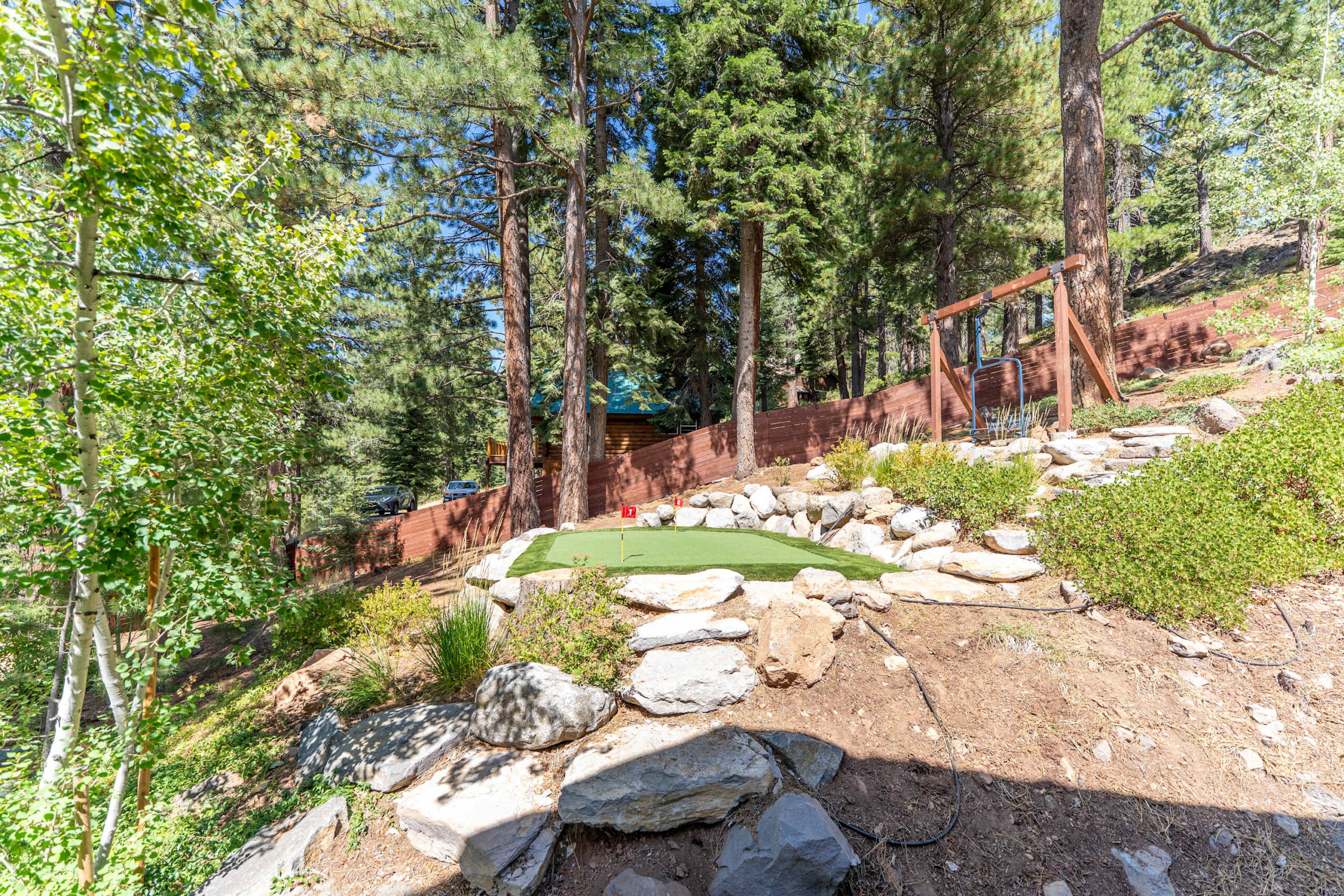 Mini-golf area in a Truckee vacation rental backyard, surrounded by trees, rocks, and greenery.