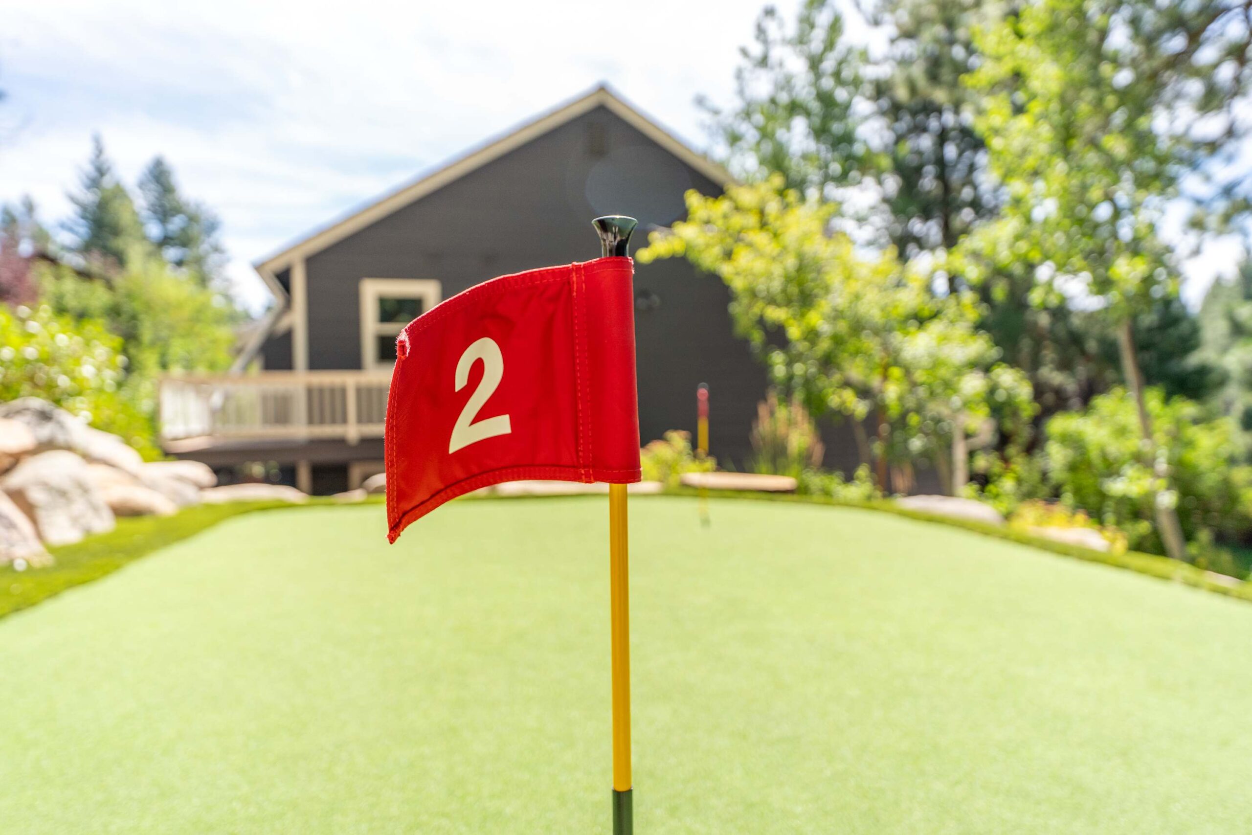 Putting green at a Truckee vacation rental, featuring a red flag with number 2 amidst lush greenery.