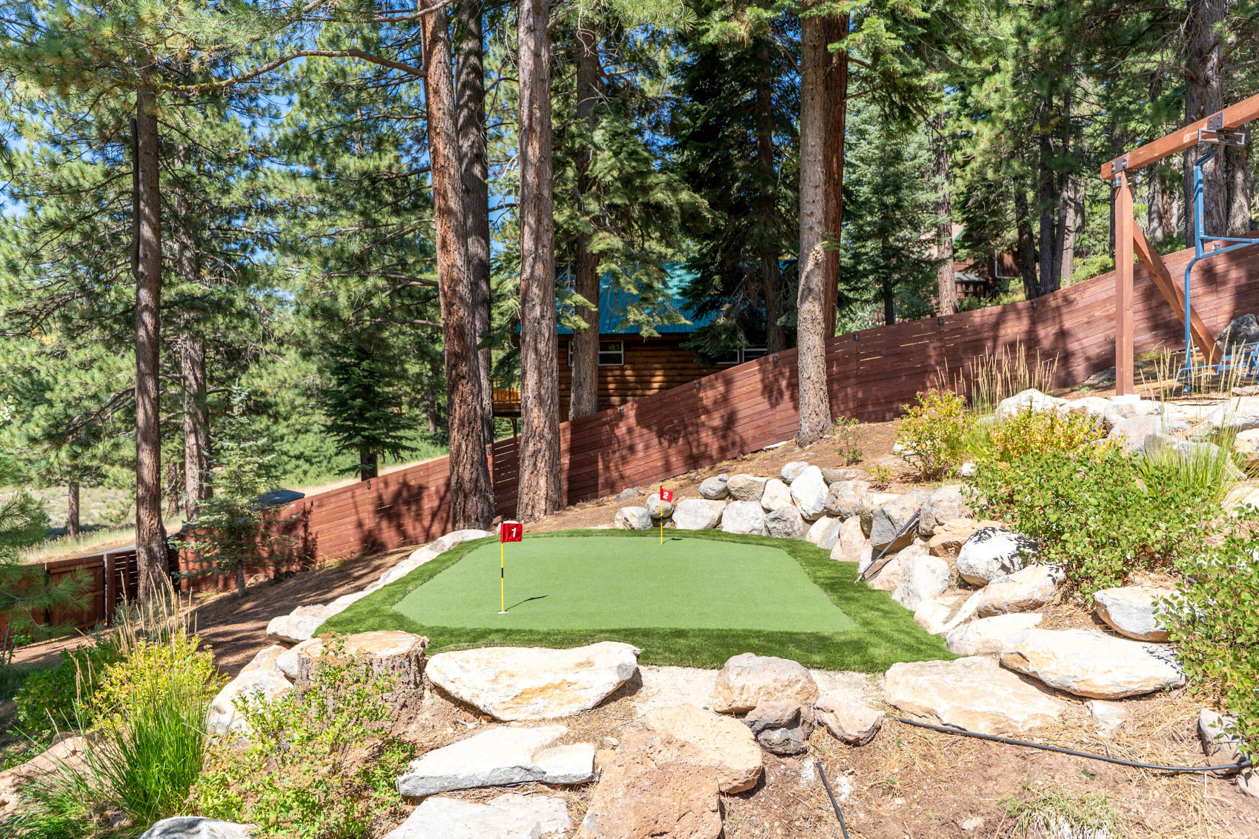 Mini-golf green at a Truckee vacation rental, surrounded by tall trees and rocks in a forested setting.