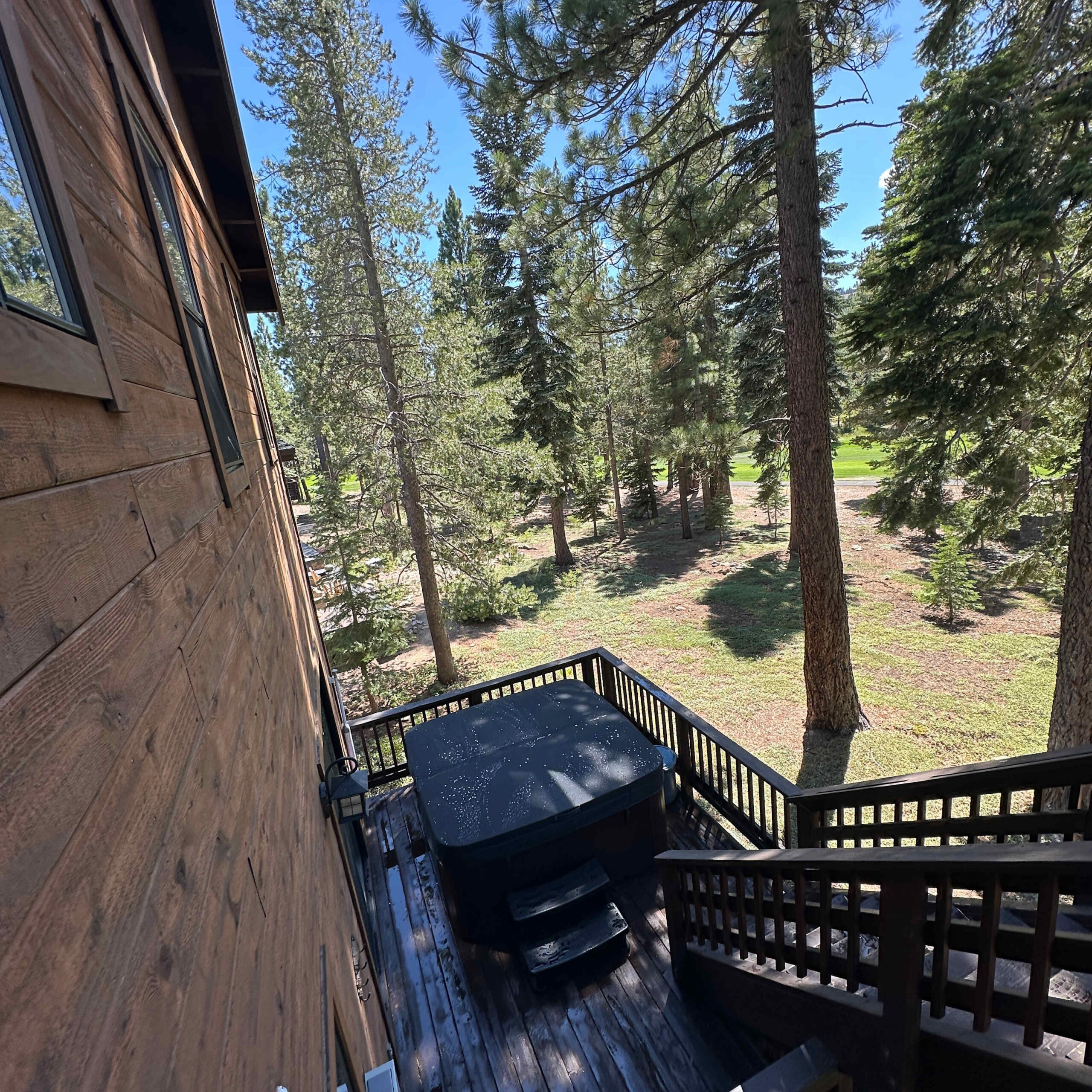 Deck with hot tub in a Truckee vacation rental, surrounded by tall trees and a wooden exterior.