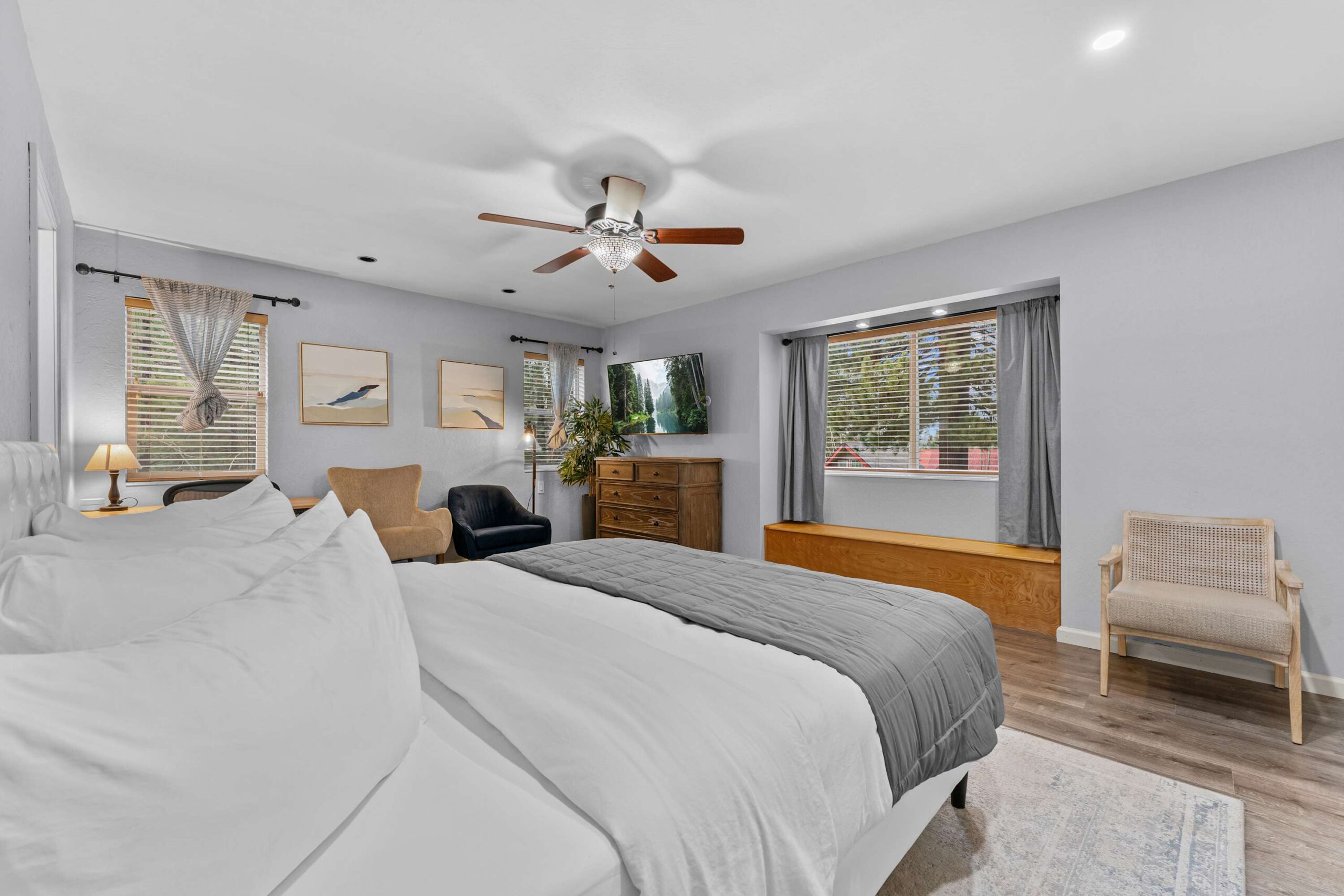 Bedroom in a Truckee vacation rental with a cozy bed, armchairs, ceiling fan, dresser, and large window with curtains.