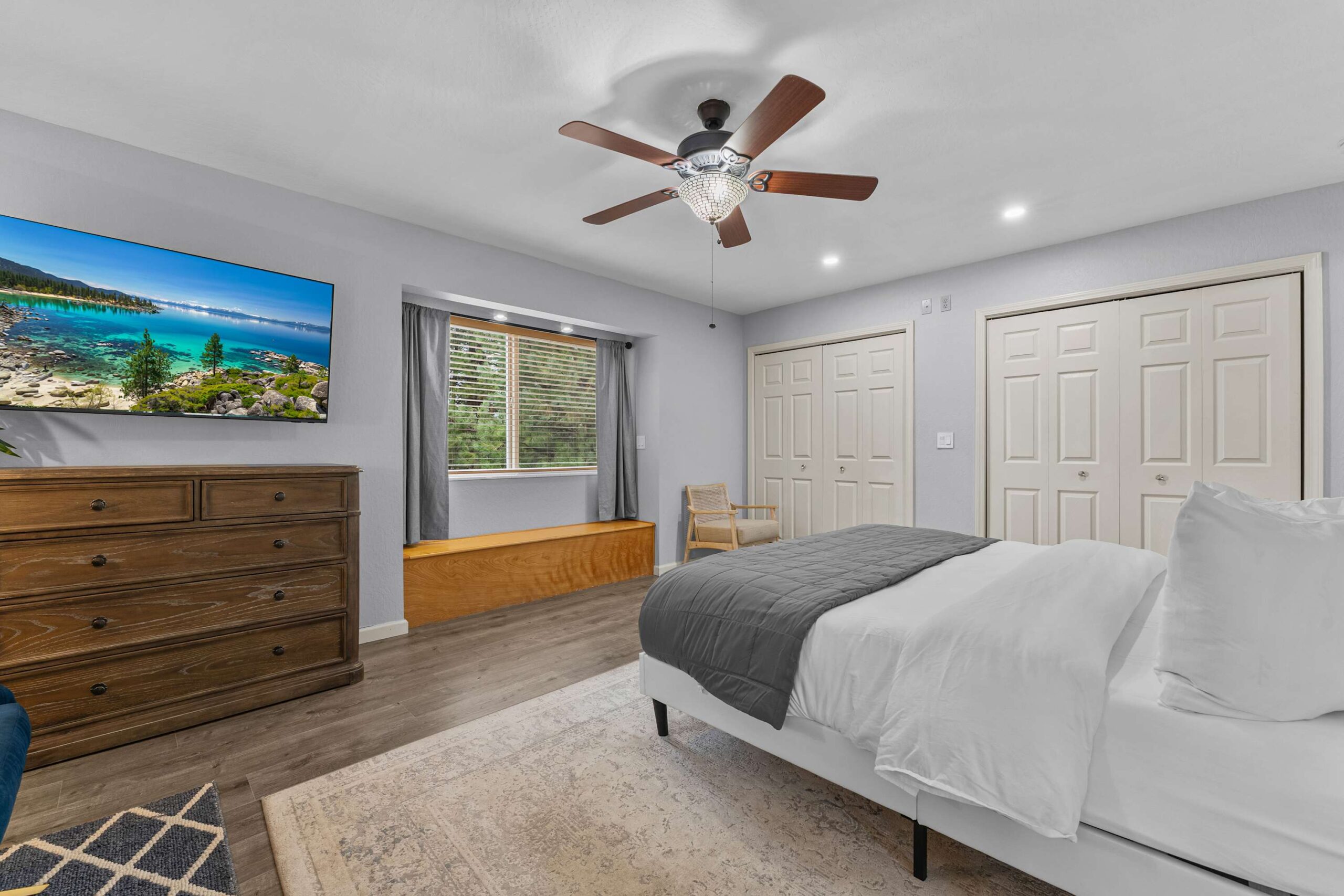 Bedroom in a Truckee vacation rental with modern decor, a cozy bed, wooden dresser, and a large window with forest views.
